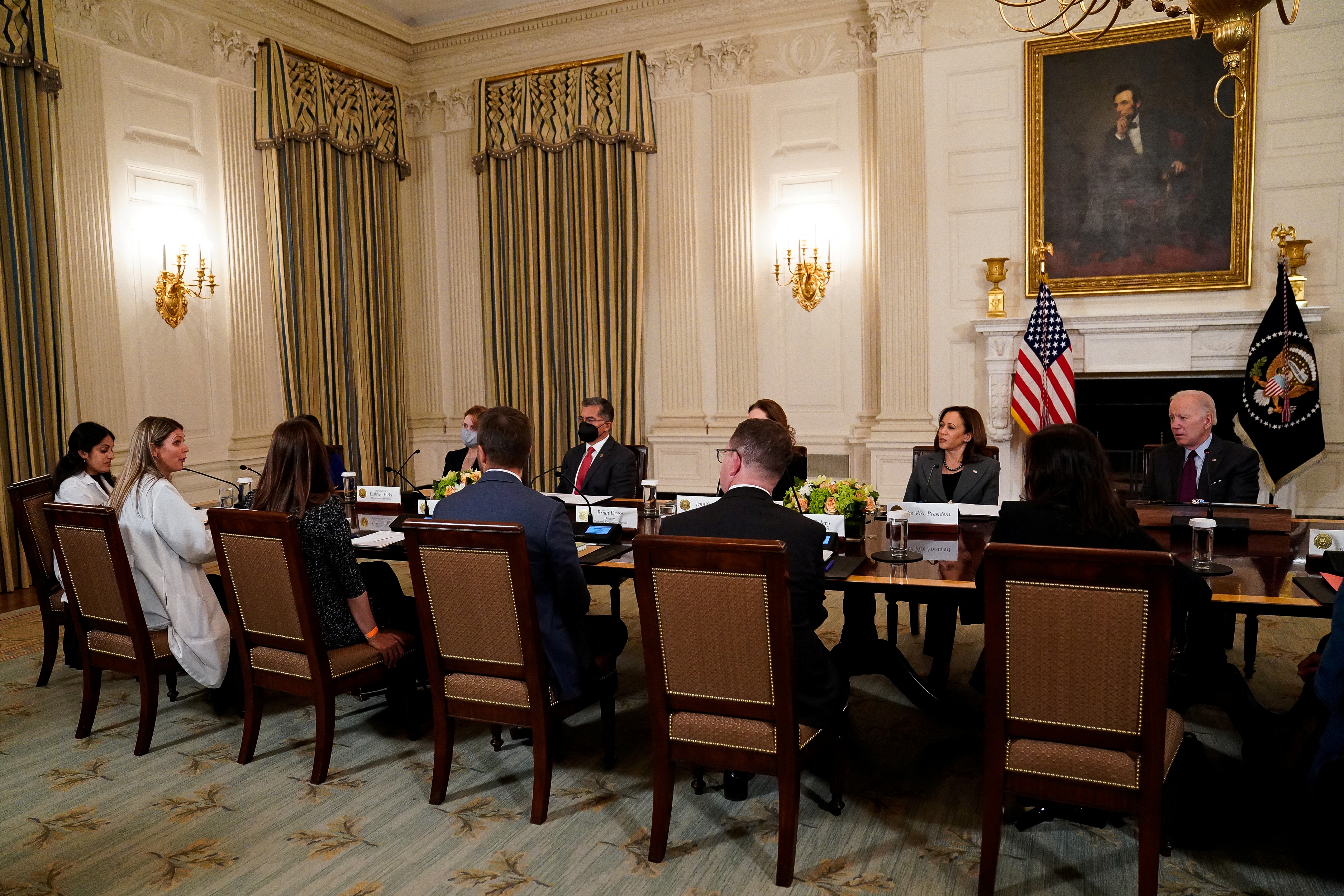 Healthcare providers sit in tall-backed chairs around a long, rectangular table in the White House, joined by President Joe Biden and Vice President Kamala Harris.