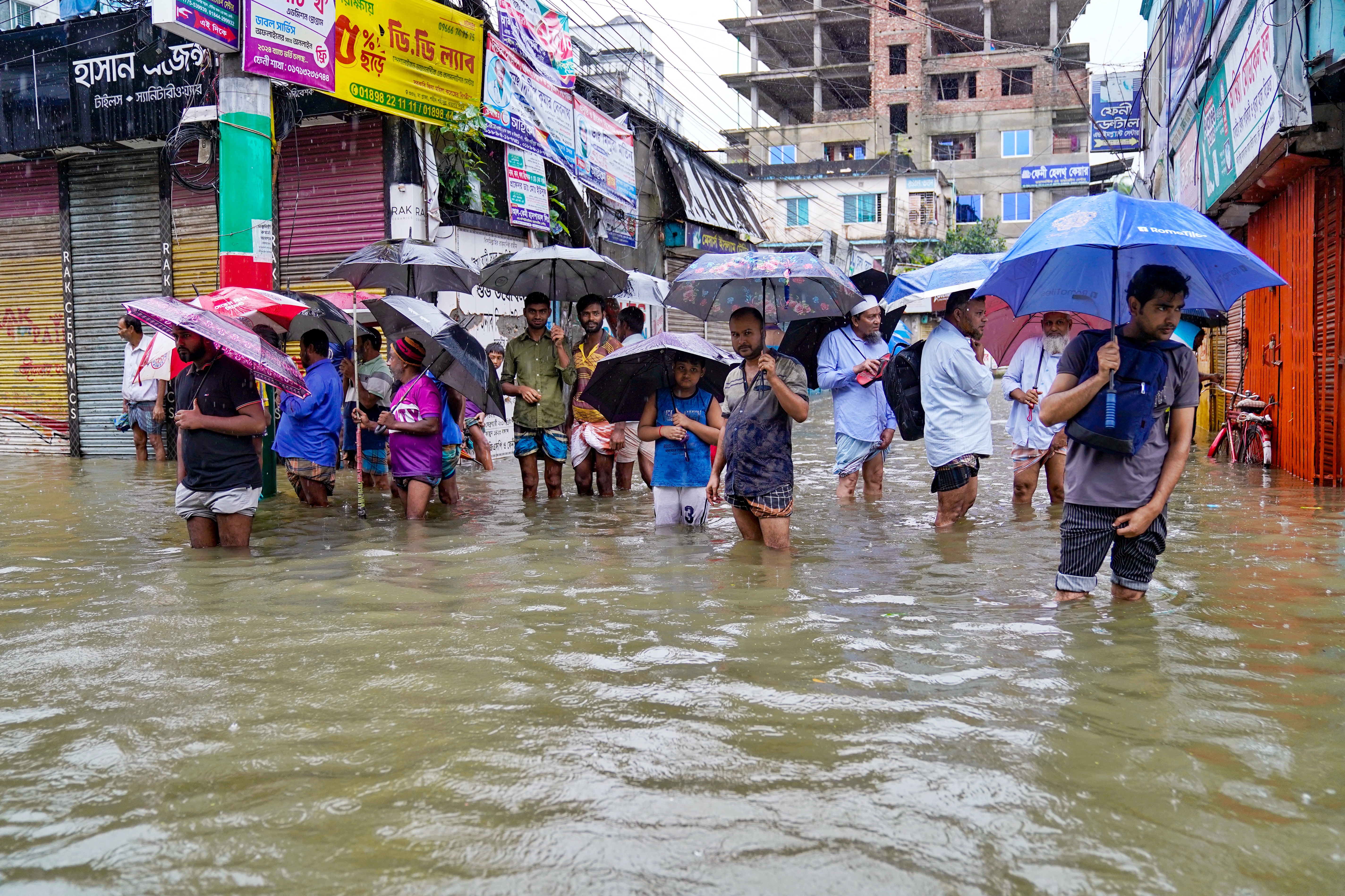 People carrying umbrellas, wade through a flooded street amid rainfall in Feni