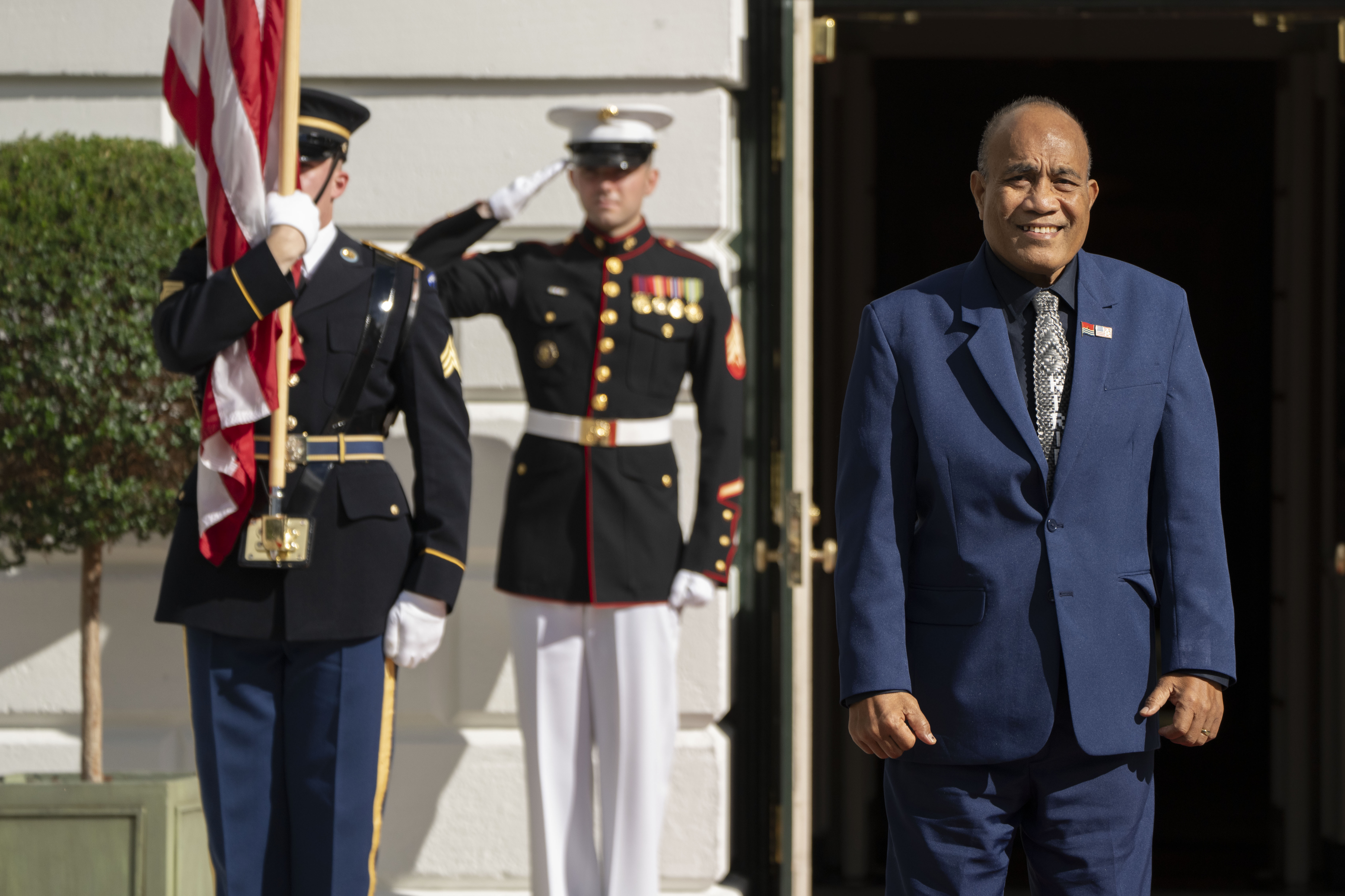 Kiribati President Taneti Maamau at the White House. There are ceremonial guards at his right shoulder. He is smiling.