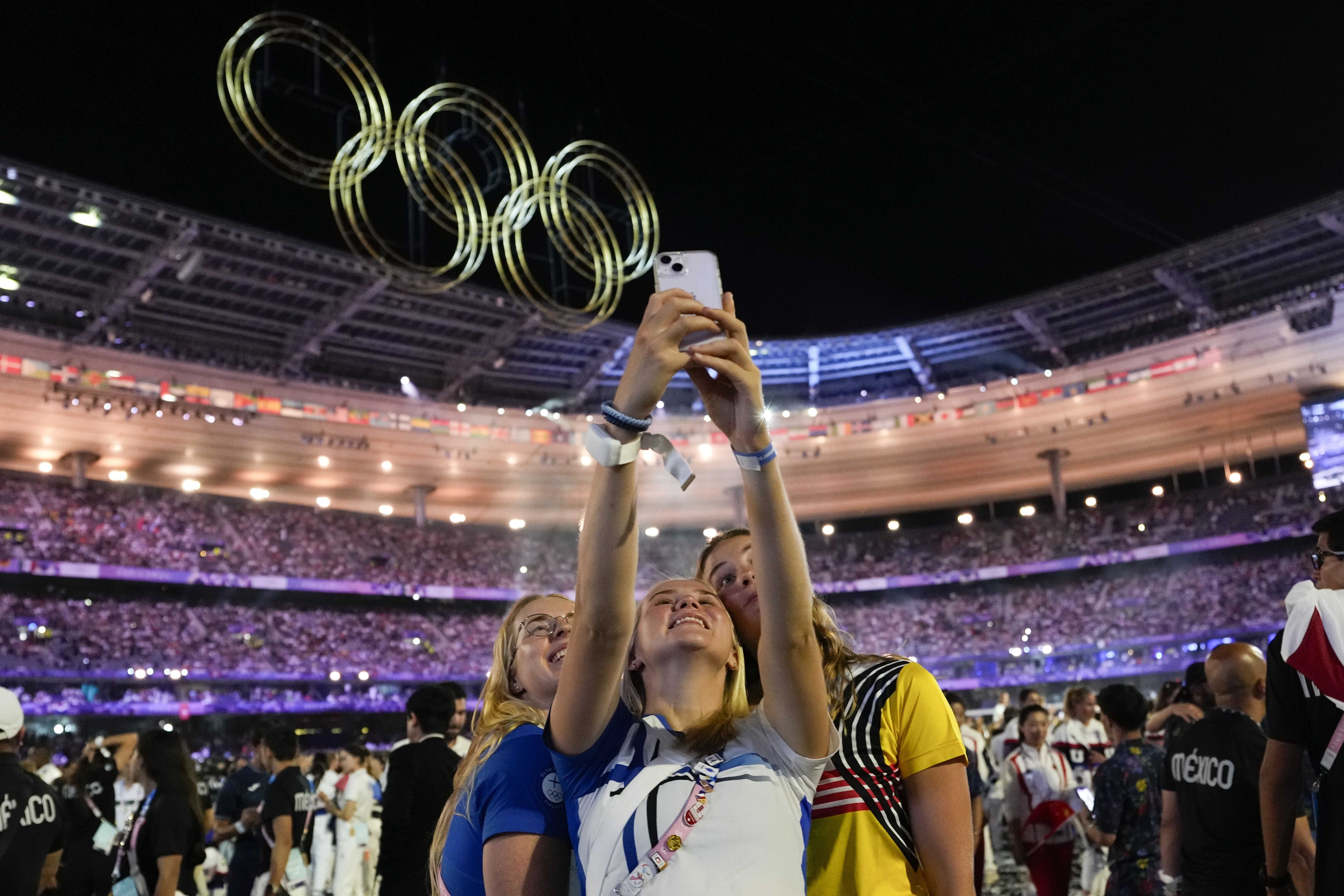 Athletes taking a selfie with the Stade de France and fireworks behind them