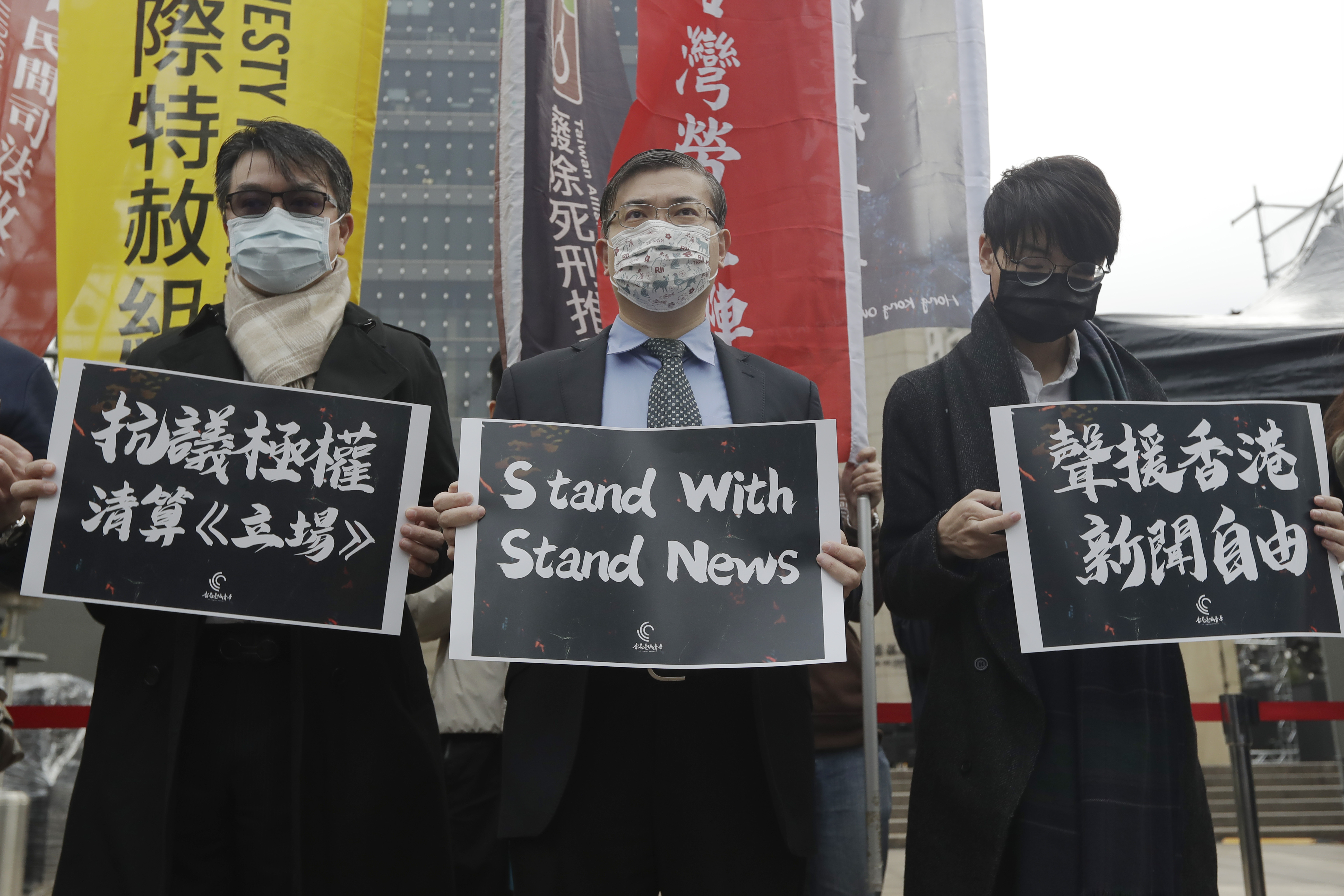 Three men rally in support of Stand News in Taiwan. They are holding banners in English and Chinese, reading 'Stand with Stand News', 'Protest against the totalitarian liquidation of Stand News' and 'Support press freedom in Hong Kong'. The men are wearing masks