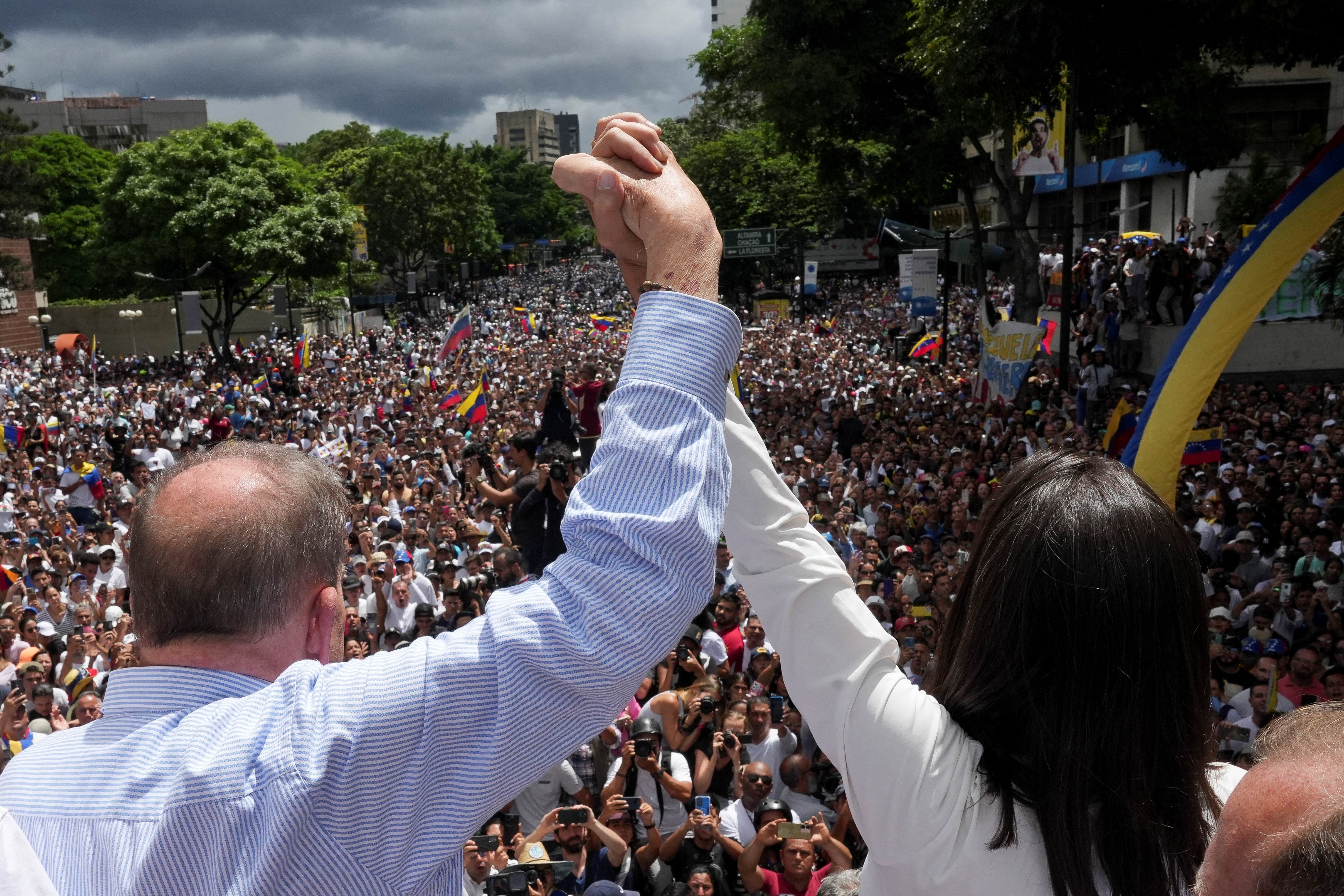 Maria Corina Machado and Edmundo Gonzalez lift up each other's hands in front of a group of protesters outside in Caracas.