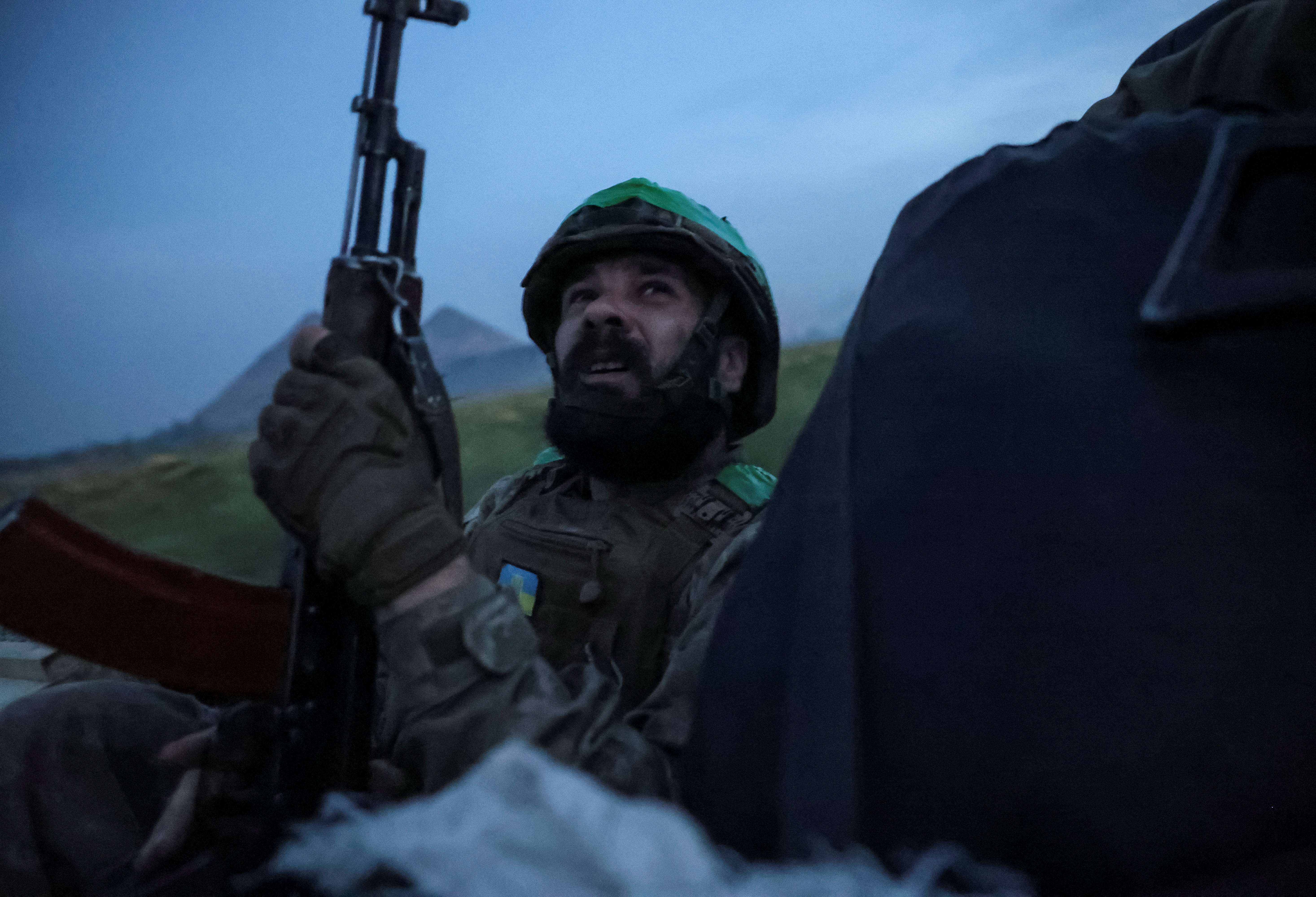 A Ukrainian soldier looking up at the sky. He is sitting in a car and has his weapon ready at his side.