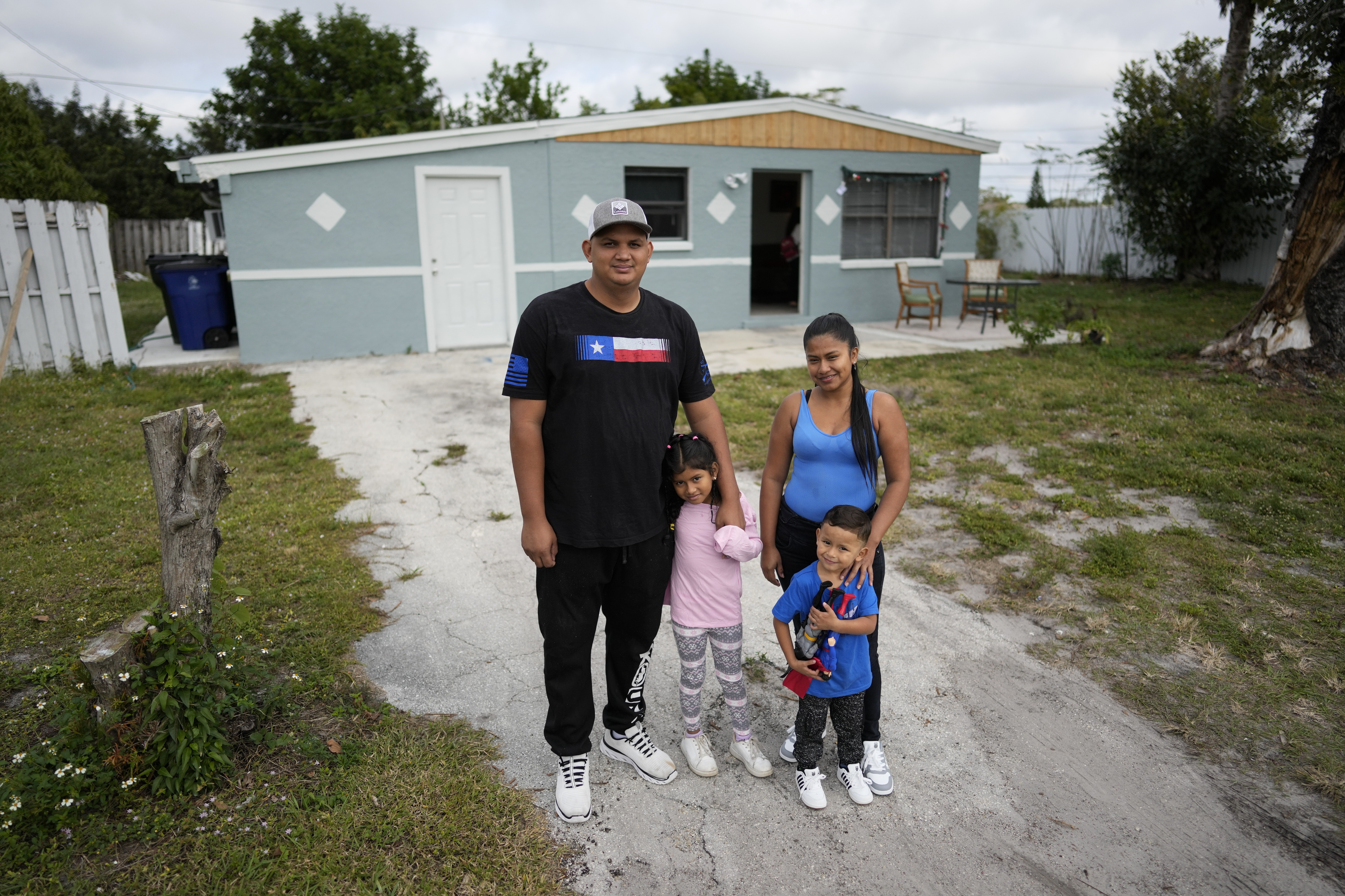 The Llanos family is among the first allowed into the United States under the "Safe Mobility Initiative." The family stands in front of a low-slung house.