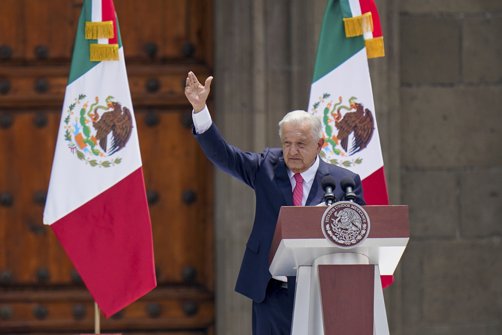 AMLO, standing in front of two Mexican flags, raises hand