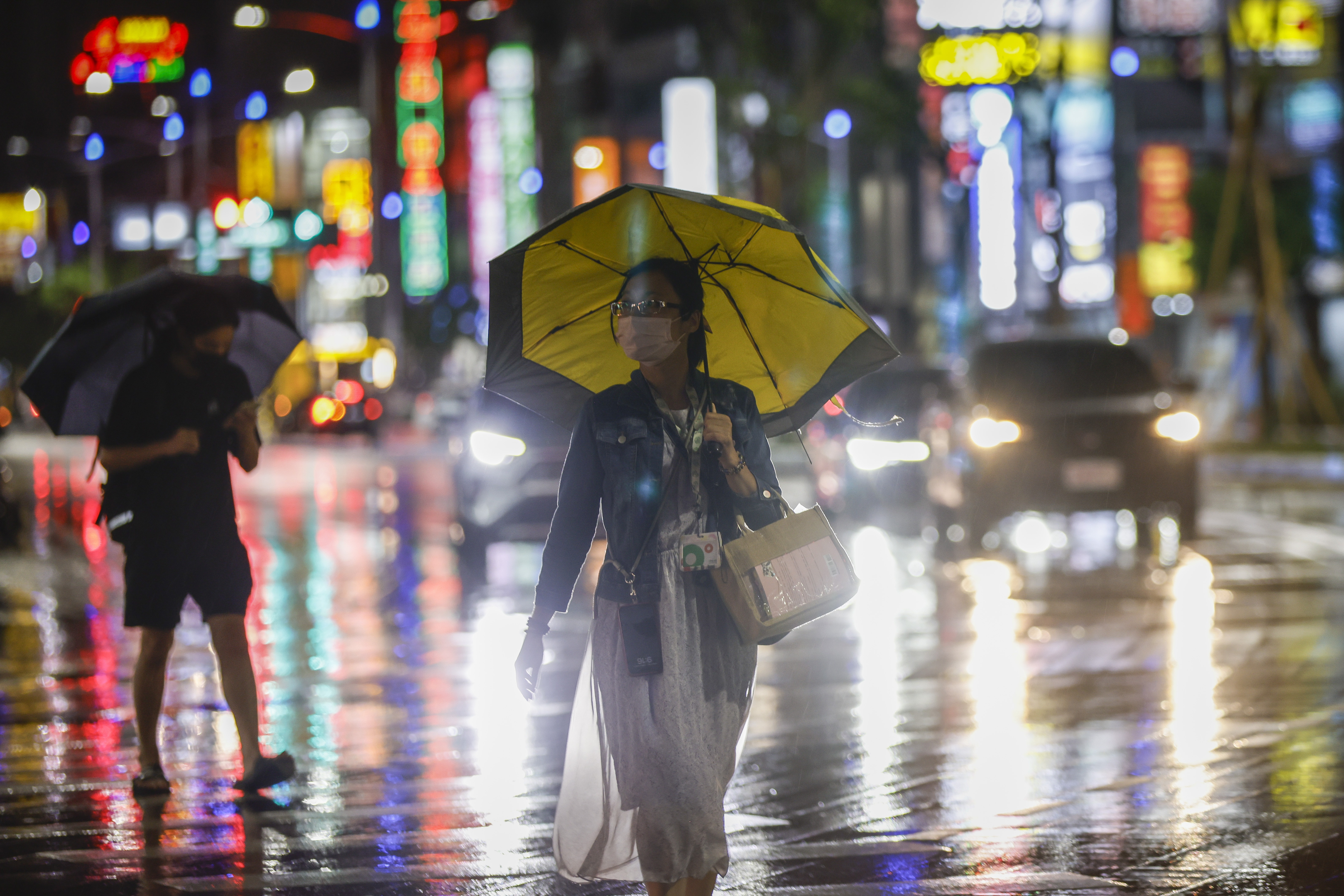 A woman with an umbrella walking in the city at night. It's raining heavily. The city lights are illuminated behind her.