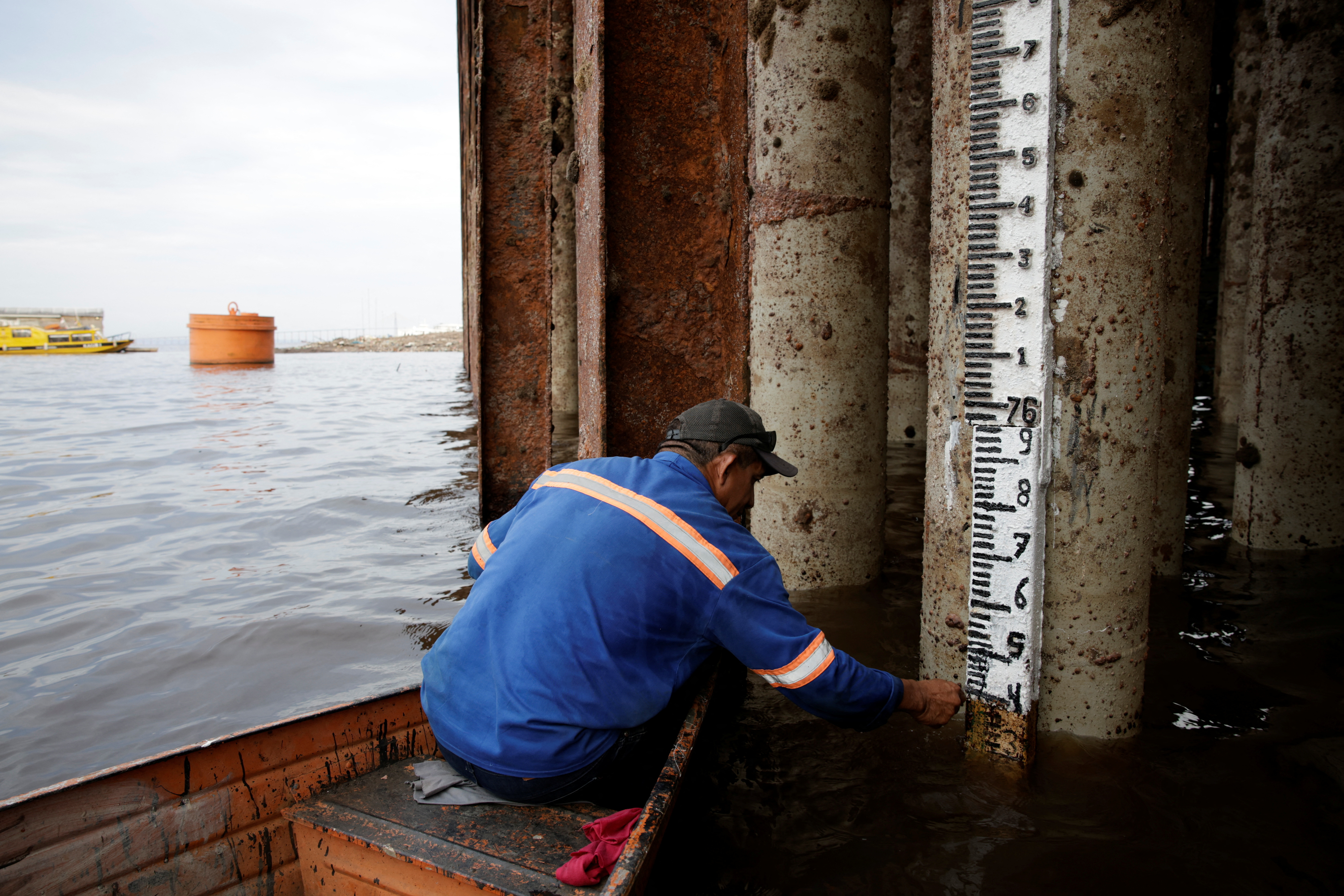 A port worker takes measurements below a pier, where a measuring stick has been placed on a piling.