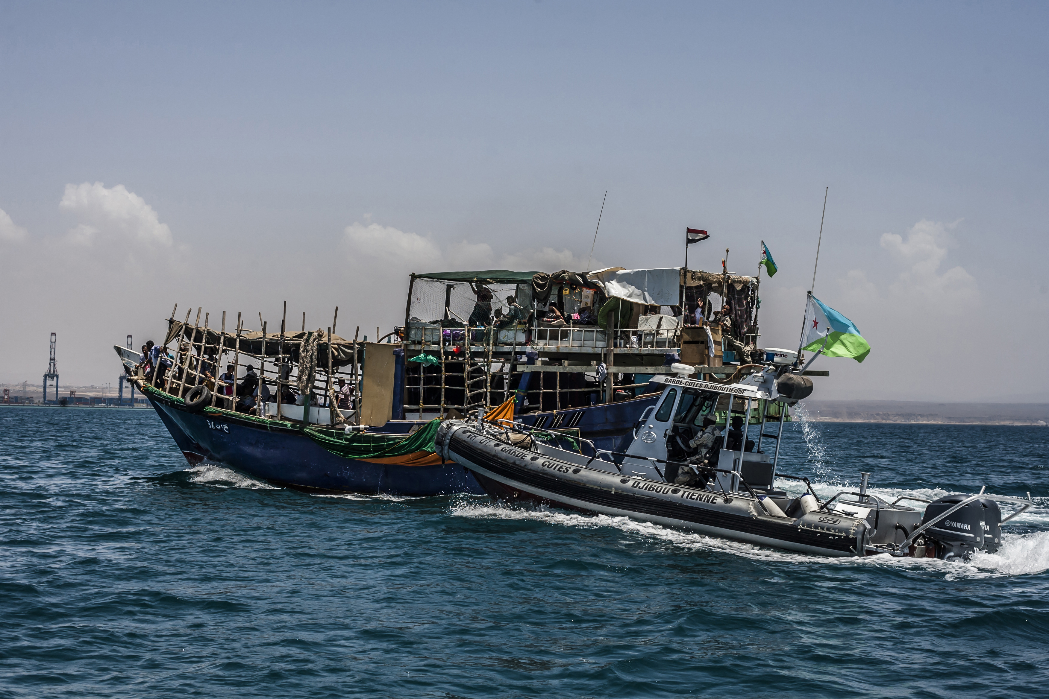 Refugees fleeing Yemen on a boat are escorted by a Djiboutian Coast Guard's vessel as they arrive in Djibouti on May 26, 2015. Since Djibouti is the only neighboring country that accept refugees, many people cross the ocean between the two countries. Almost 2,000 people have been killed and more than half a million displaced in Yemen since the fighting escalated in March with the Saudi-led coalition launching air war against the Huthis in an effort to restore the authority of President Abderabbo Mansour al-Hadi, who has fled to Riyadh after the rebels overran most of the country. AFP PHOTO / ANDREAS STAHL (Photo by ANDREAS STAHL / AFP)