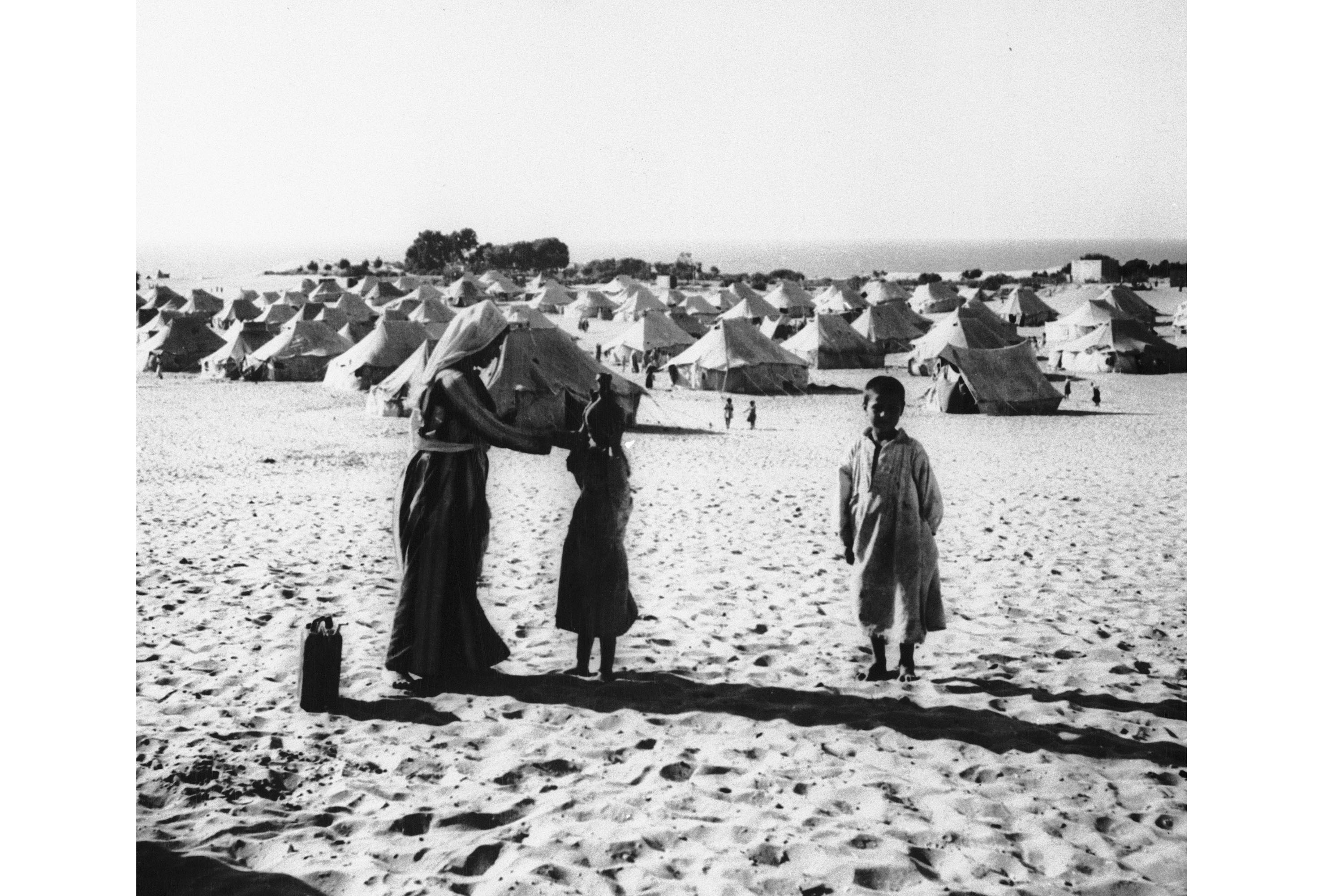 A mother and her children are seen at tent city in the Gaza area of Egyptian-occupied Palestine where about 216,000 Arab refugees live in worn-out tents, July 23, 1949. The woman is teaching her daughter how to carry a water jug on her head. (AP Photo/S. Swinton)