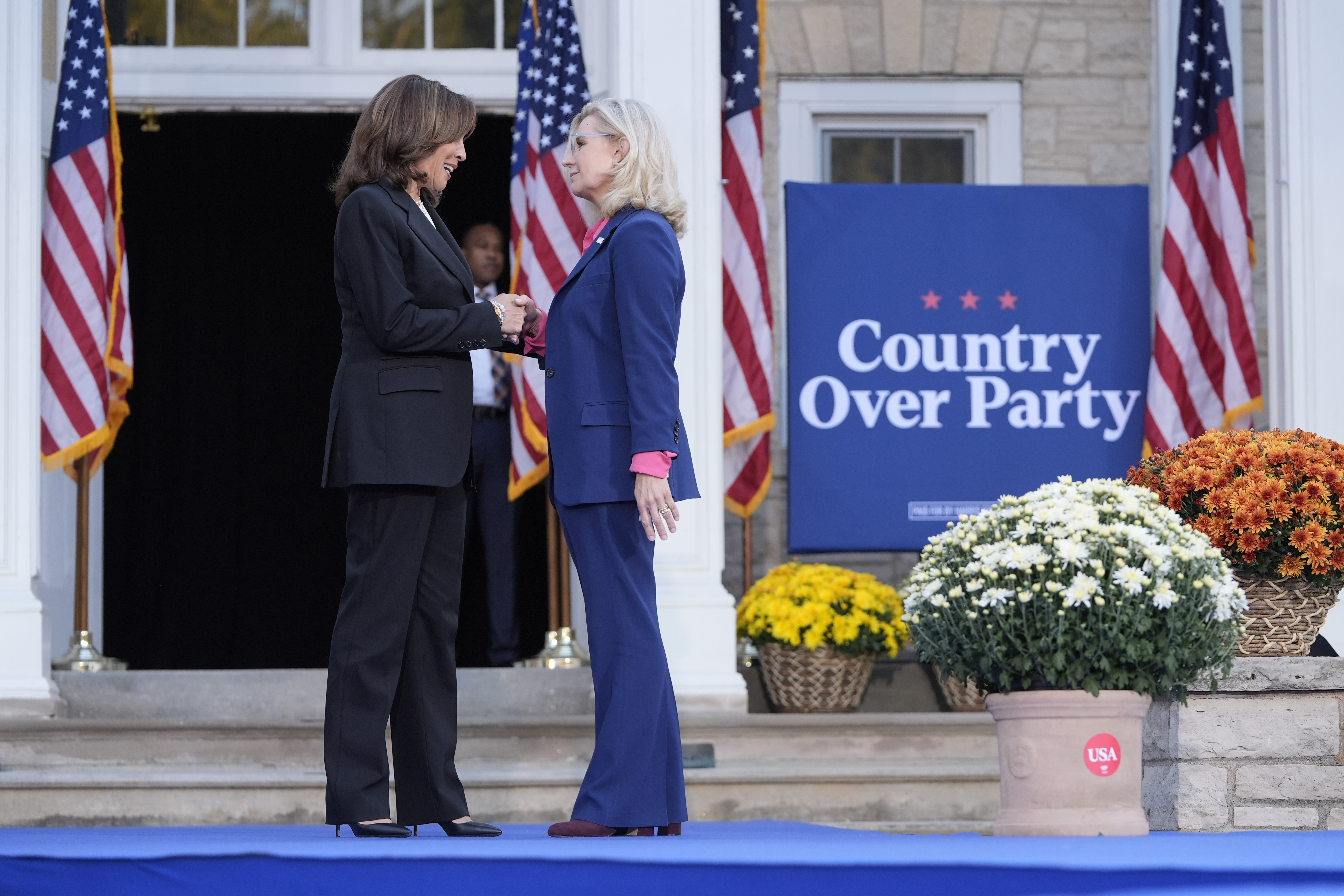Kamala Harris and Liz Cheney shake hands on stage in front of a sign that reads: "Country over Party."
