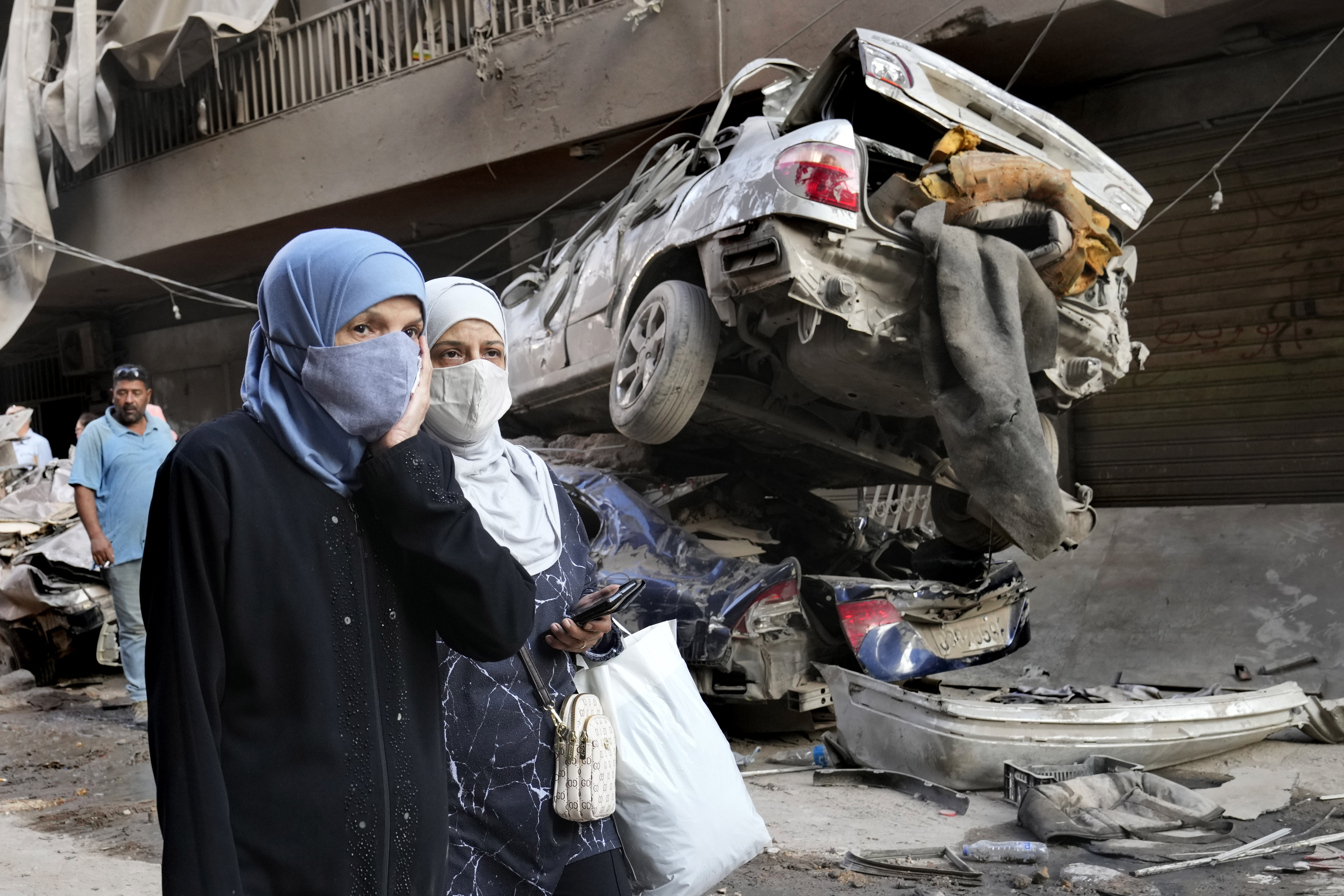 Lebanese women pass next of destroyed cars, at the site of Thursday's Israeli airstrike, in Beirut, Lebanon, Friday, Oct. 11