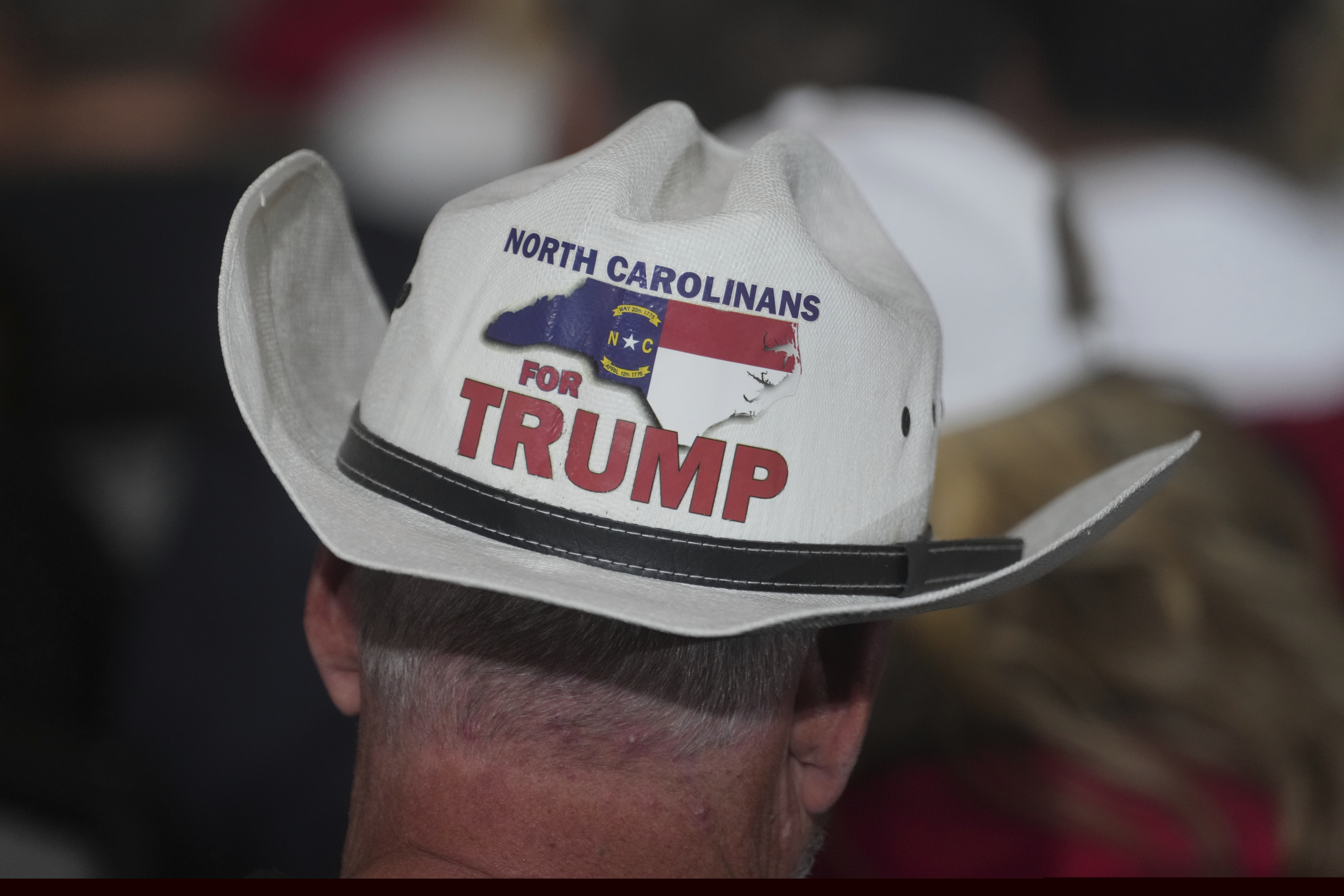 A man wears a cowboy hat that reads "North Carolinians for Trump" on the back
