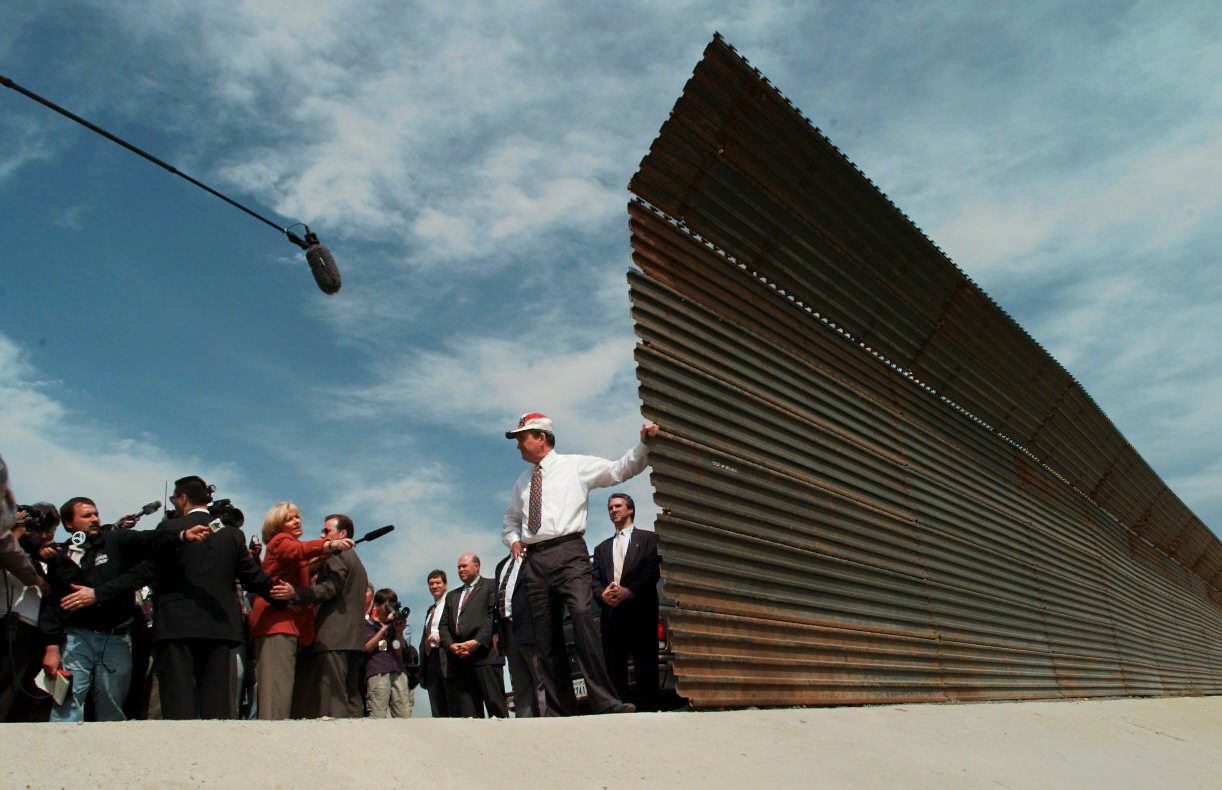 Pat Buchanan poses, leaning against the US-Mexico border wall in the 1990s.