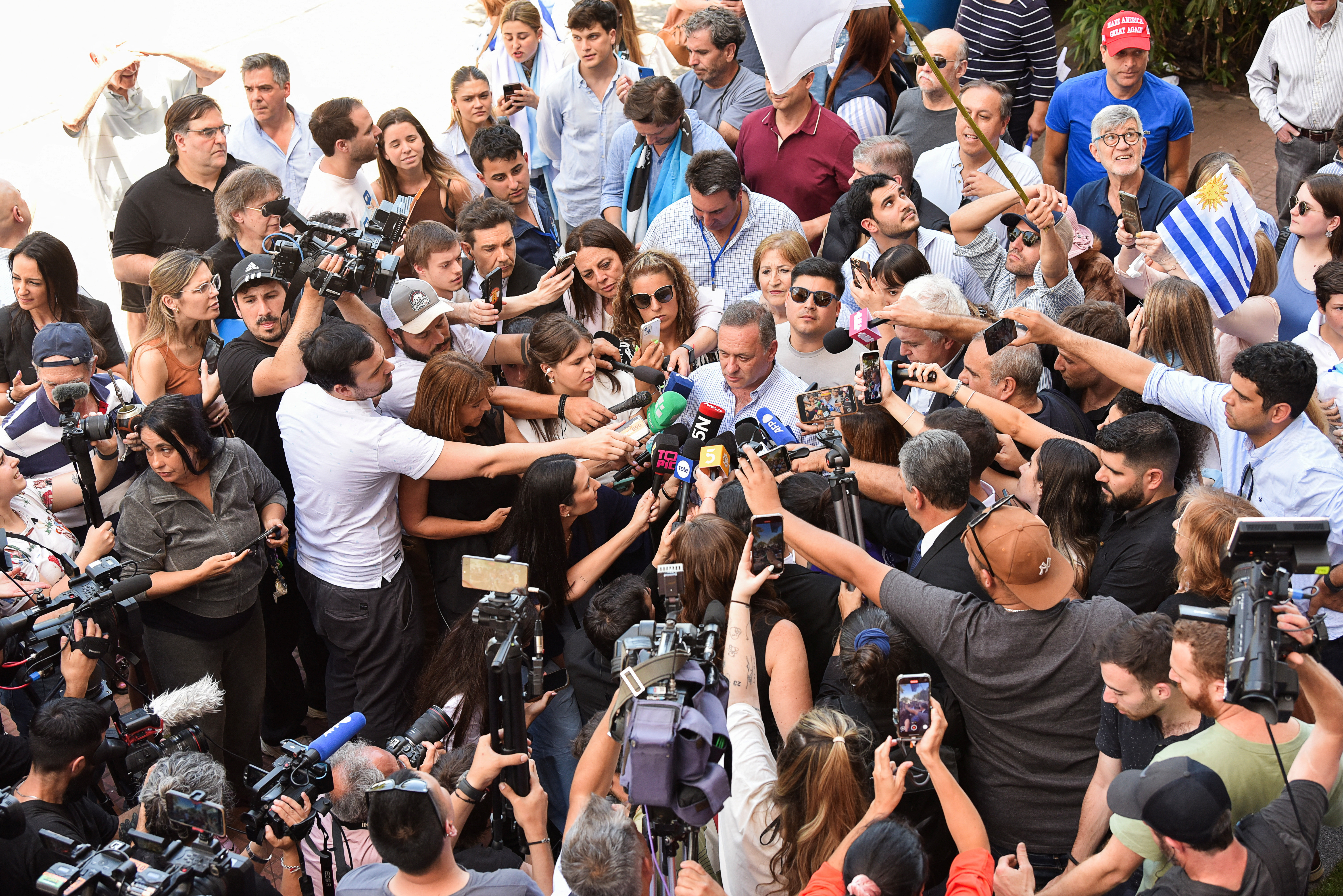 Alvaro Delgado is surrounded by a scrum of reporters all holding their microphones to him.