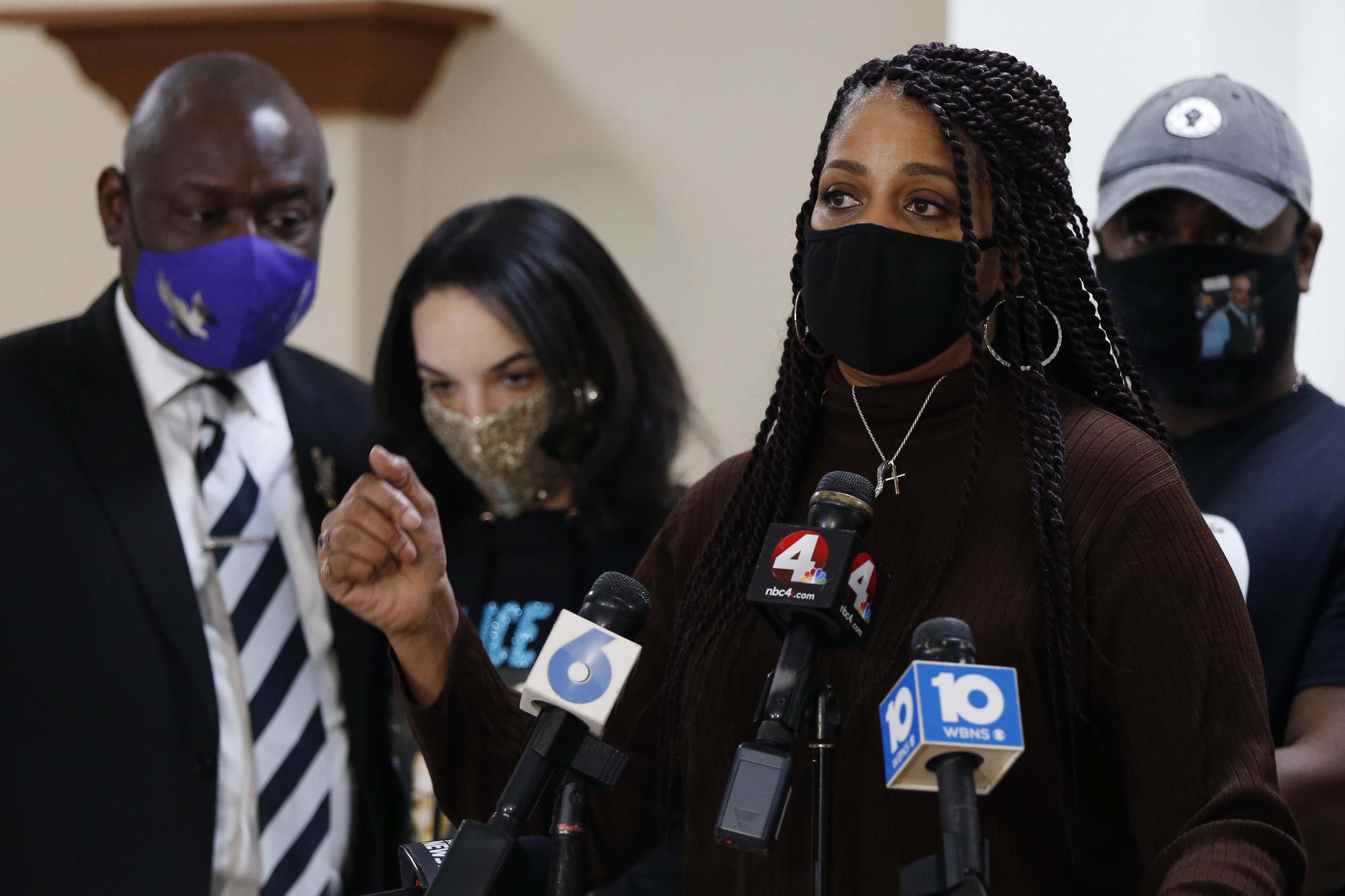 Sister of Andre Hill speaks into a microphone surrounded by family