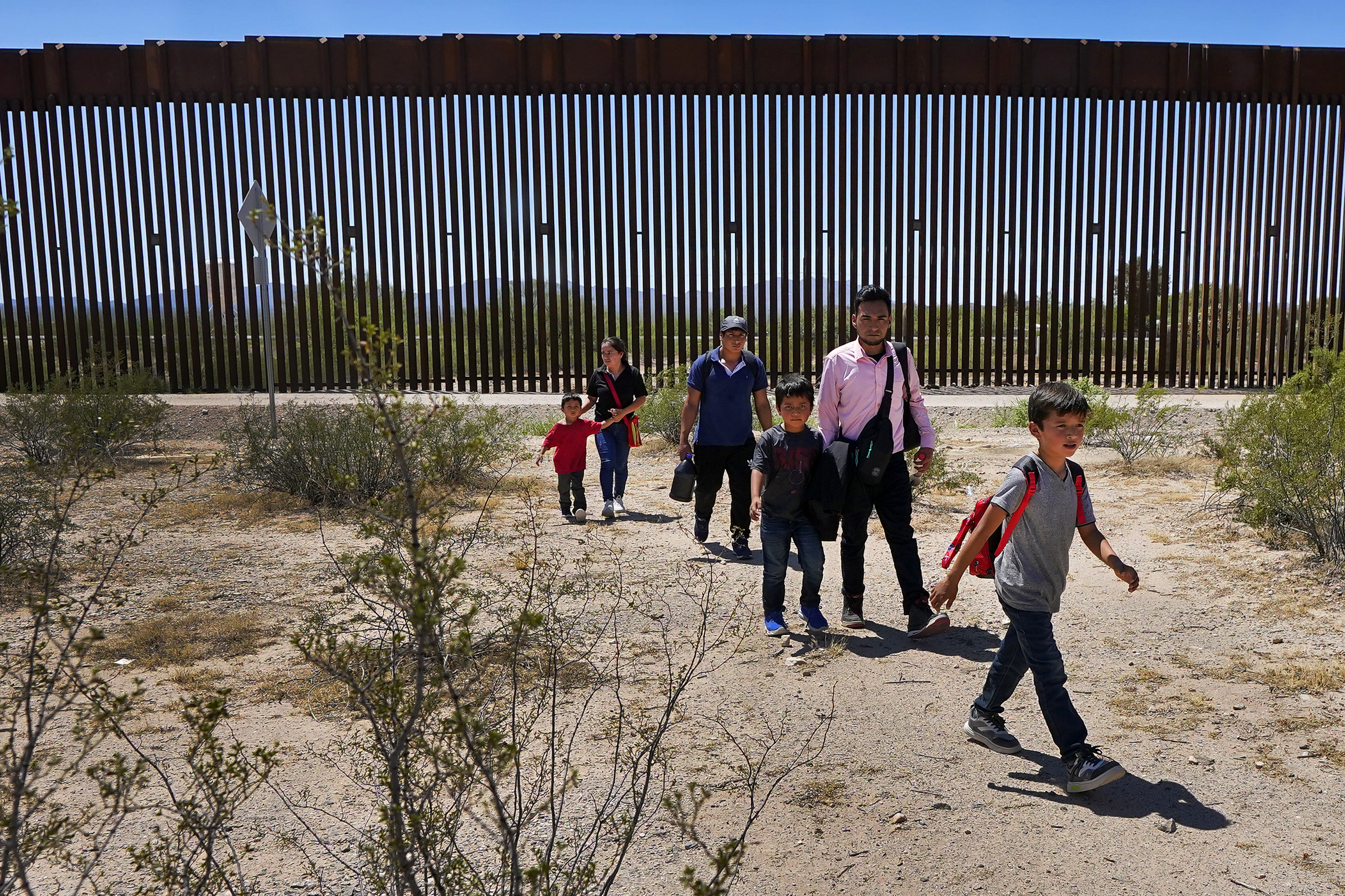 A family of migrants and asylum seekers cross the US-Mexico border wall on their way into the US
