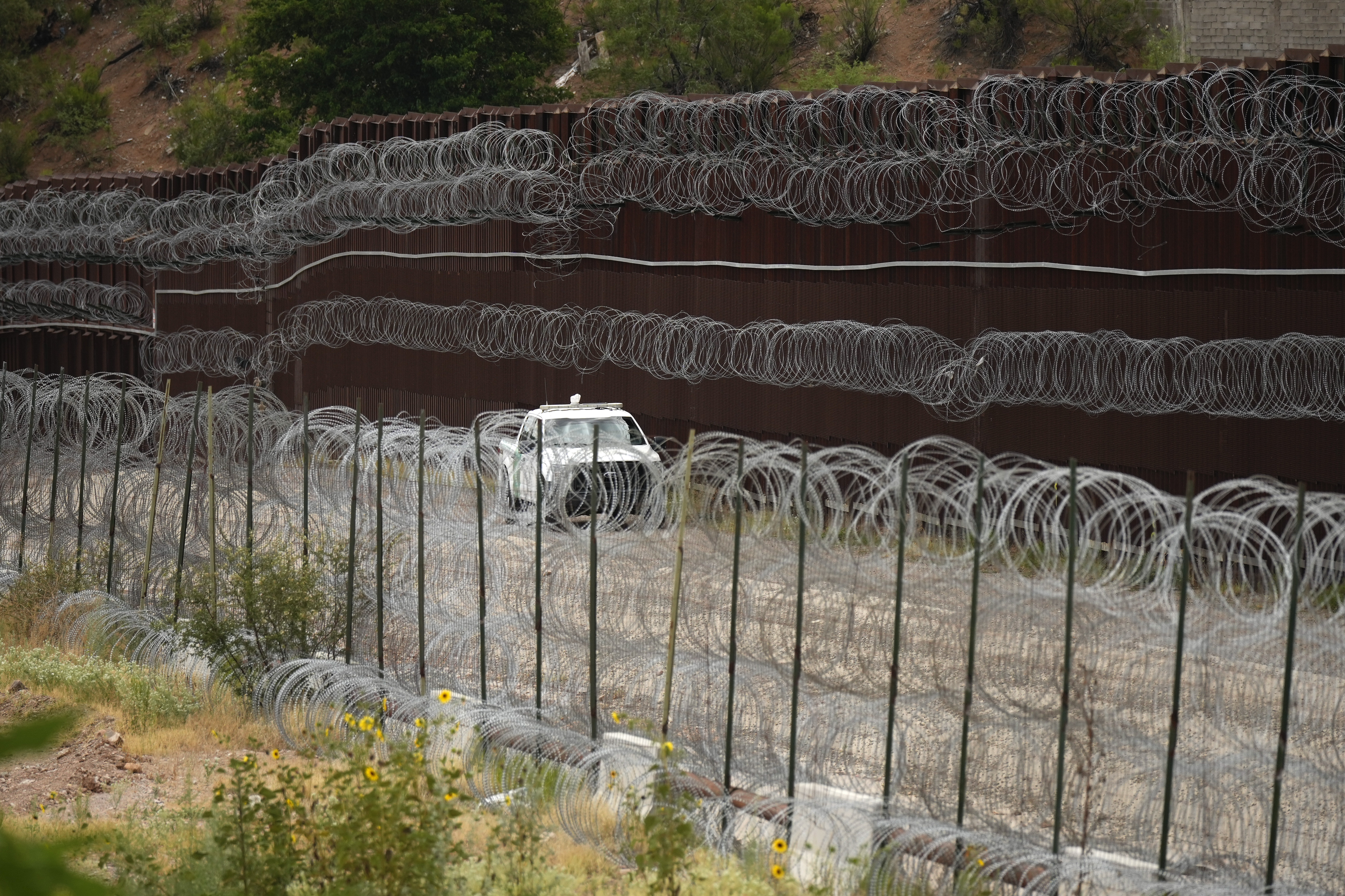 A truck drives alongside a razor-wire lined fence at the US-Mexico border