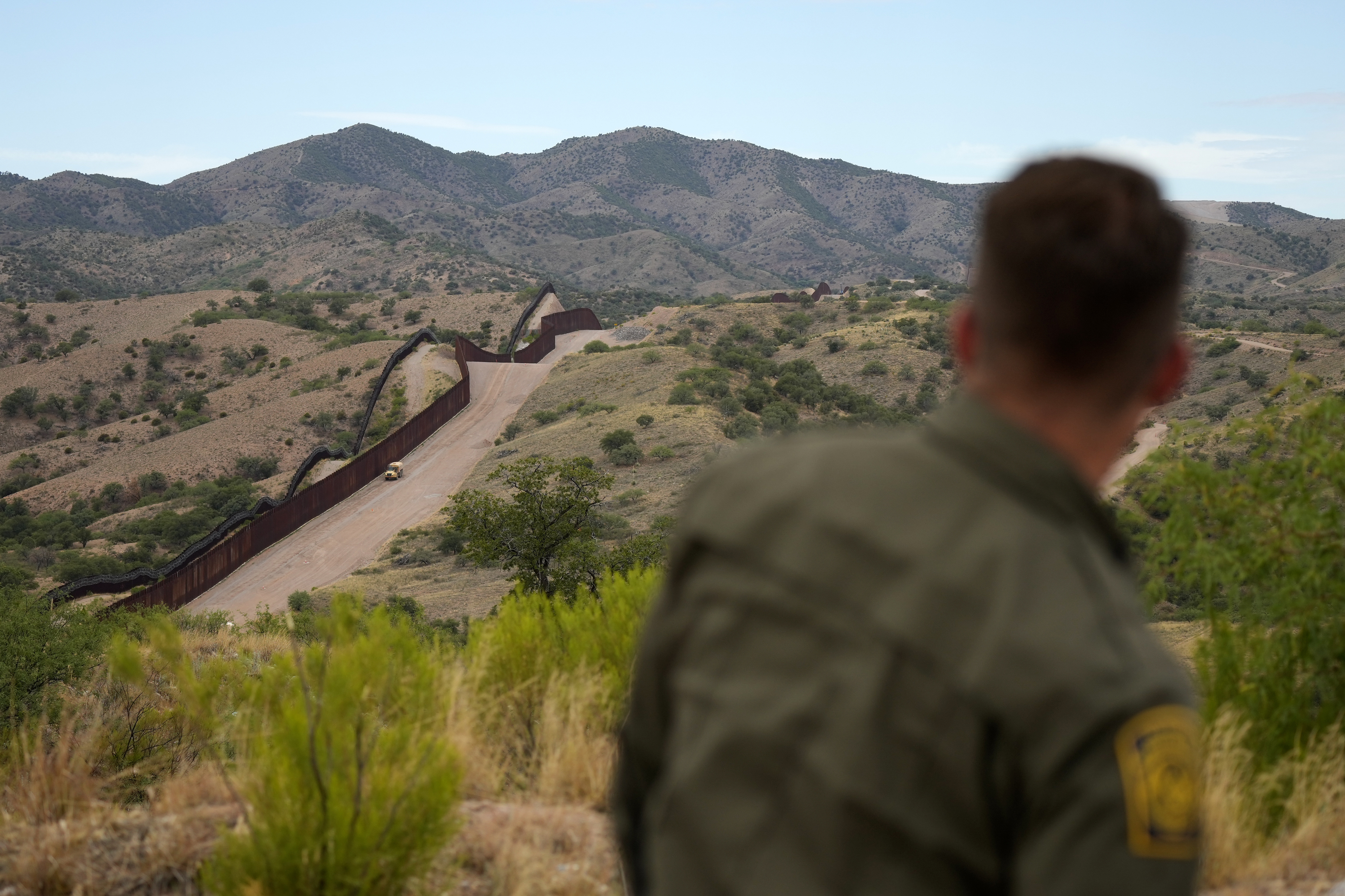 A border patrol agent looks down from a hilltop onto the barrier separating the US and Mexico.