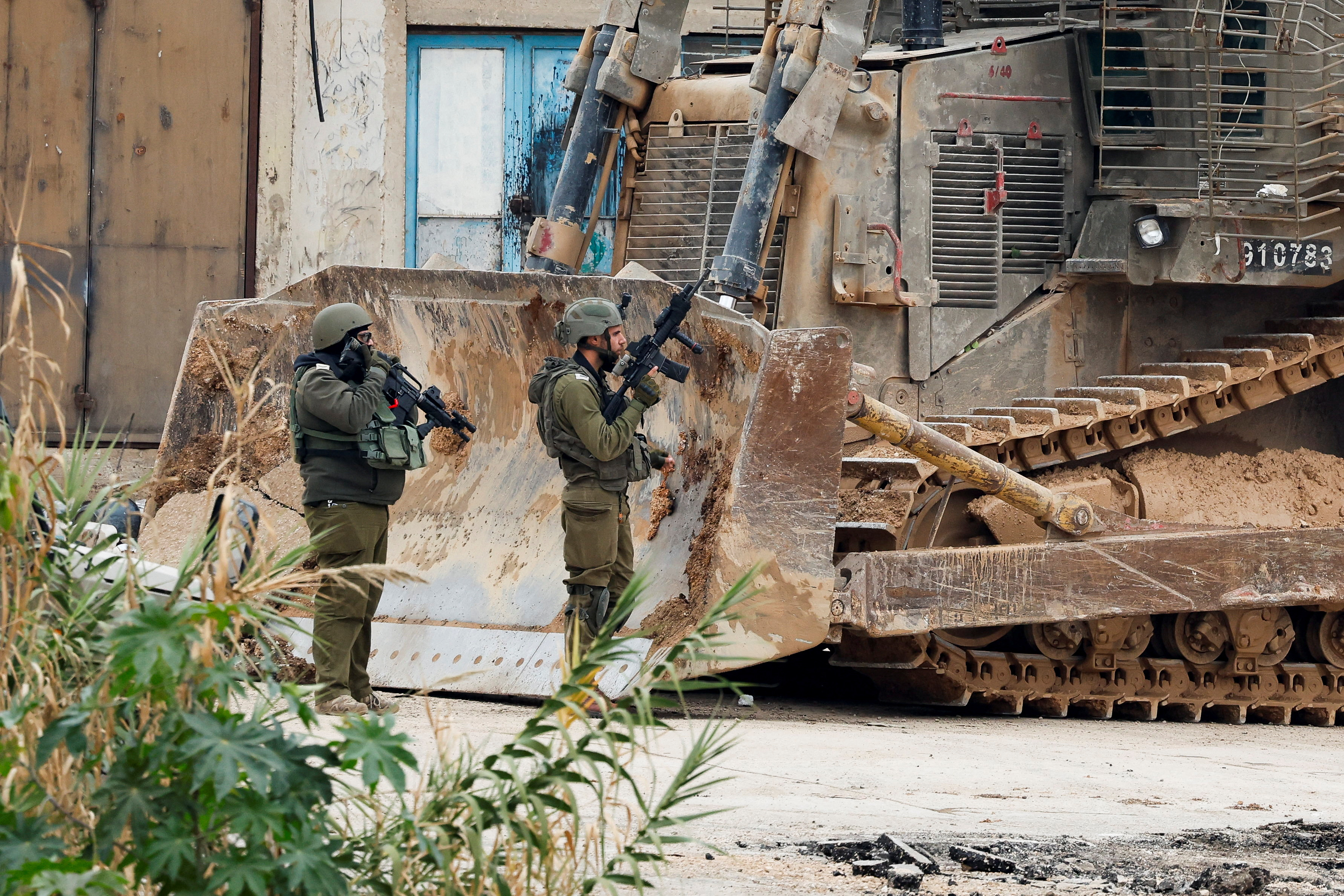 two soldiers stand next to an armoured bulldozer