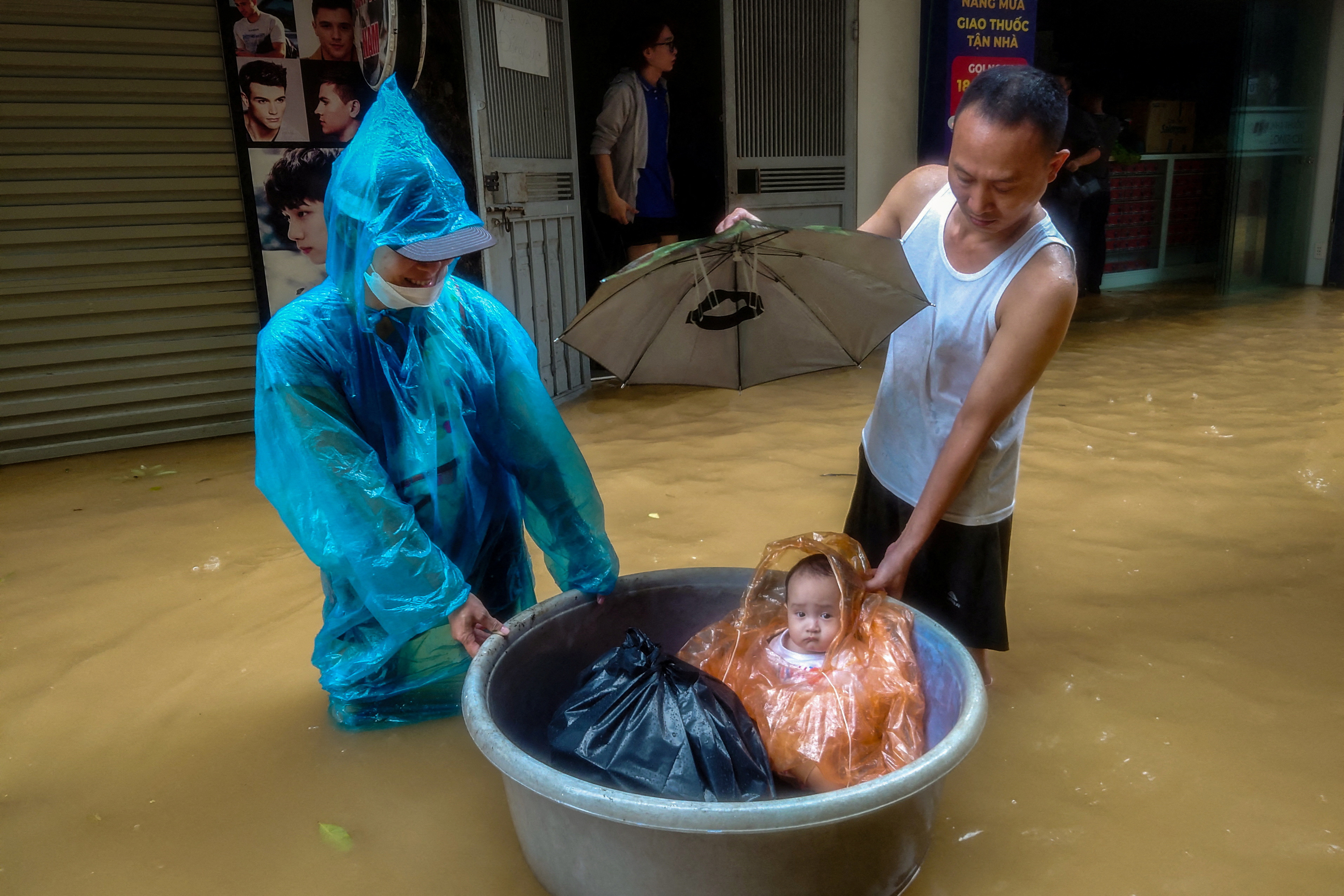 A boy sits in a floating basket as people wade through a flooded street following the impact of Typhoon Yagi, in Hanoi, Vietnam, September 11, 2024
