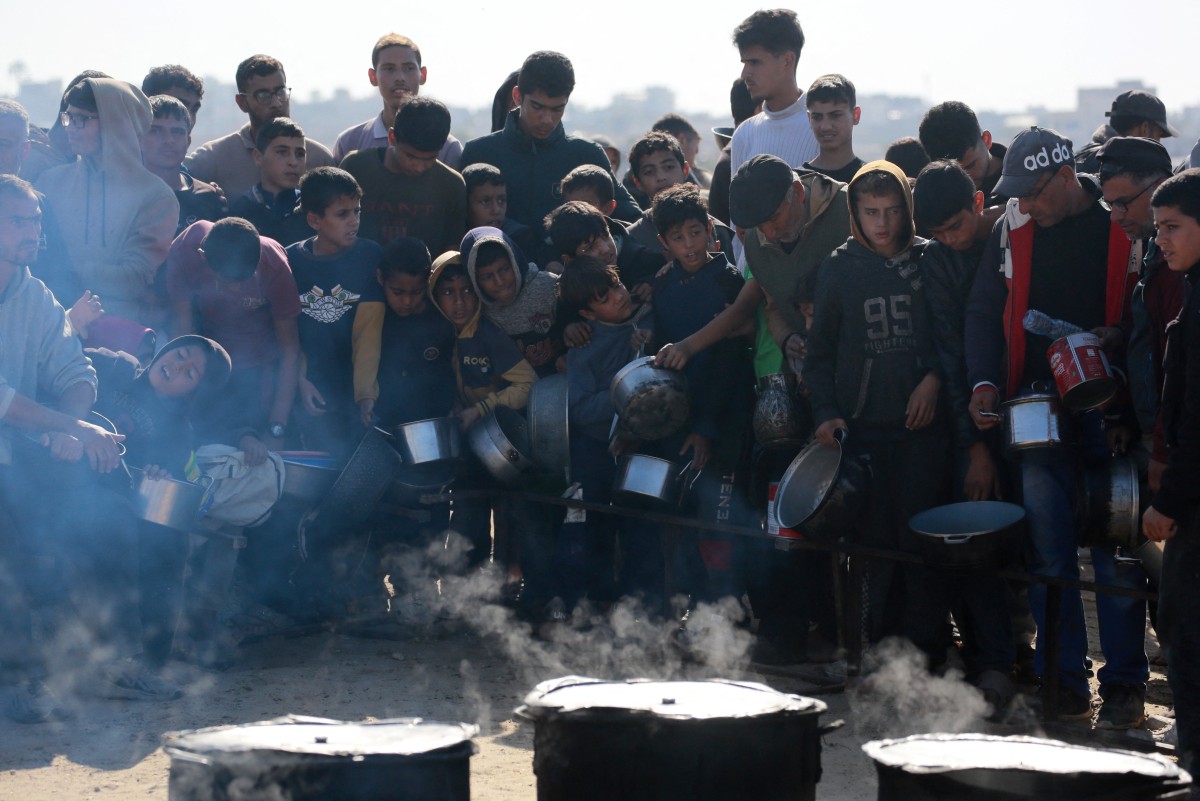 Palestinians stand in wait for a food portion at a distribution centre south of Khan Yunis in the southern Gaza Strip on December 17, 2024, amid the ongoing war between Israel and the Palestinian Hamas movement. (Photo by BASHAR TALEB / AFP)