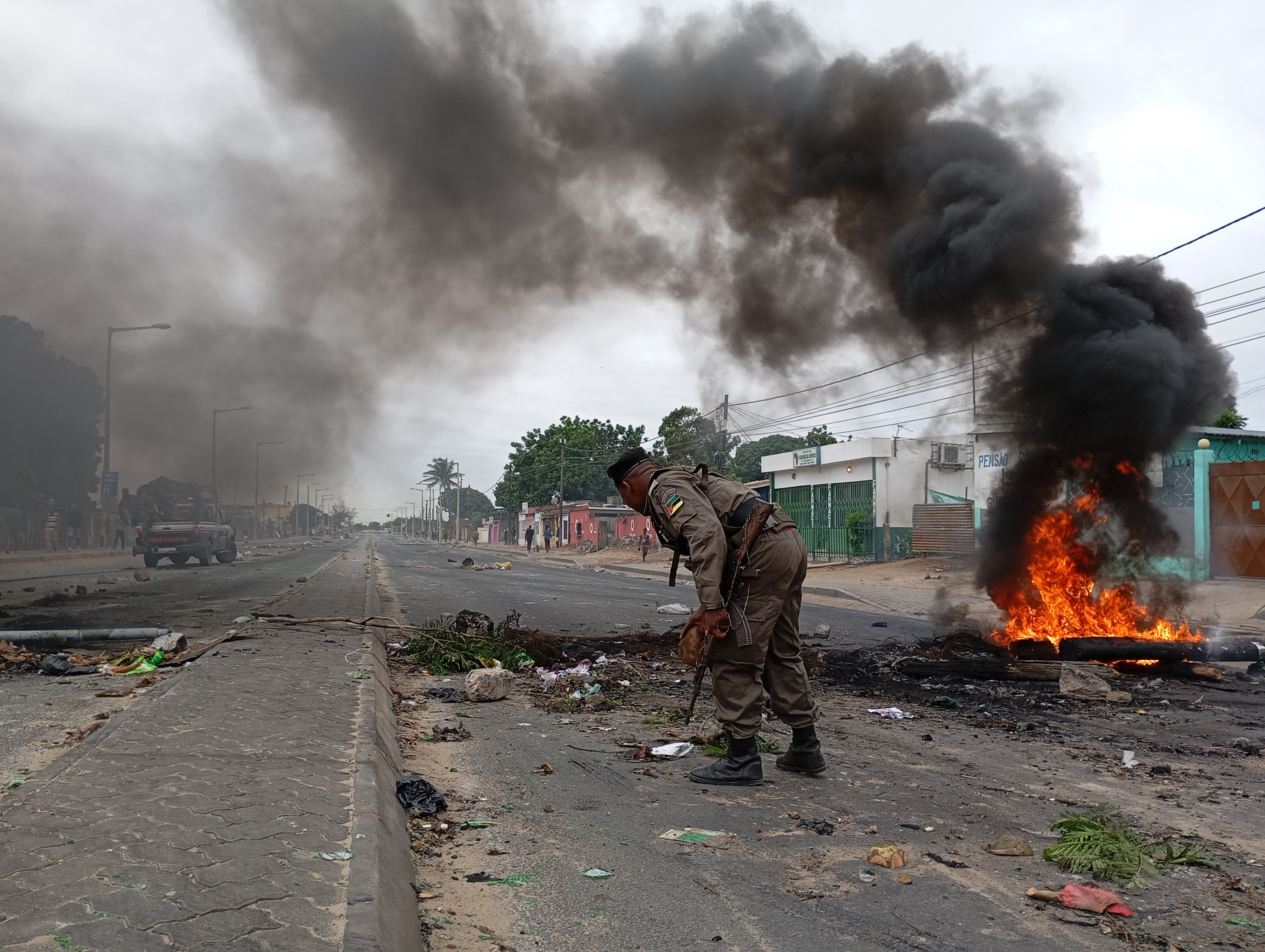 Mozambican security forces are seen next to a burning barricade in Maputo on December 24, 2024. - The capital of Mozambique was deserted on Tuesday, its main arteries heavily secured, noted AFP, the day after the confirmation of the victory in the October elections of Frelimo, in power for half a century, while the opposition maintains his denunciations of fraud. Maputo remains frozen in a climate of fear and insecurity on Christmas Eve after violent demonstrations in the evening and night. The police, in armored vehicles, patrol the center.