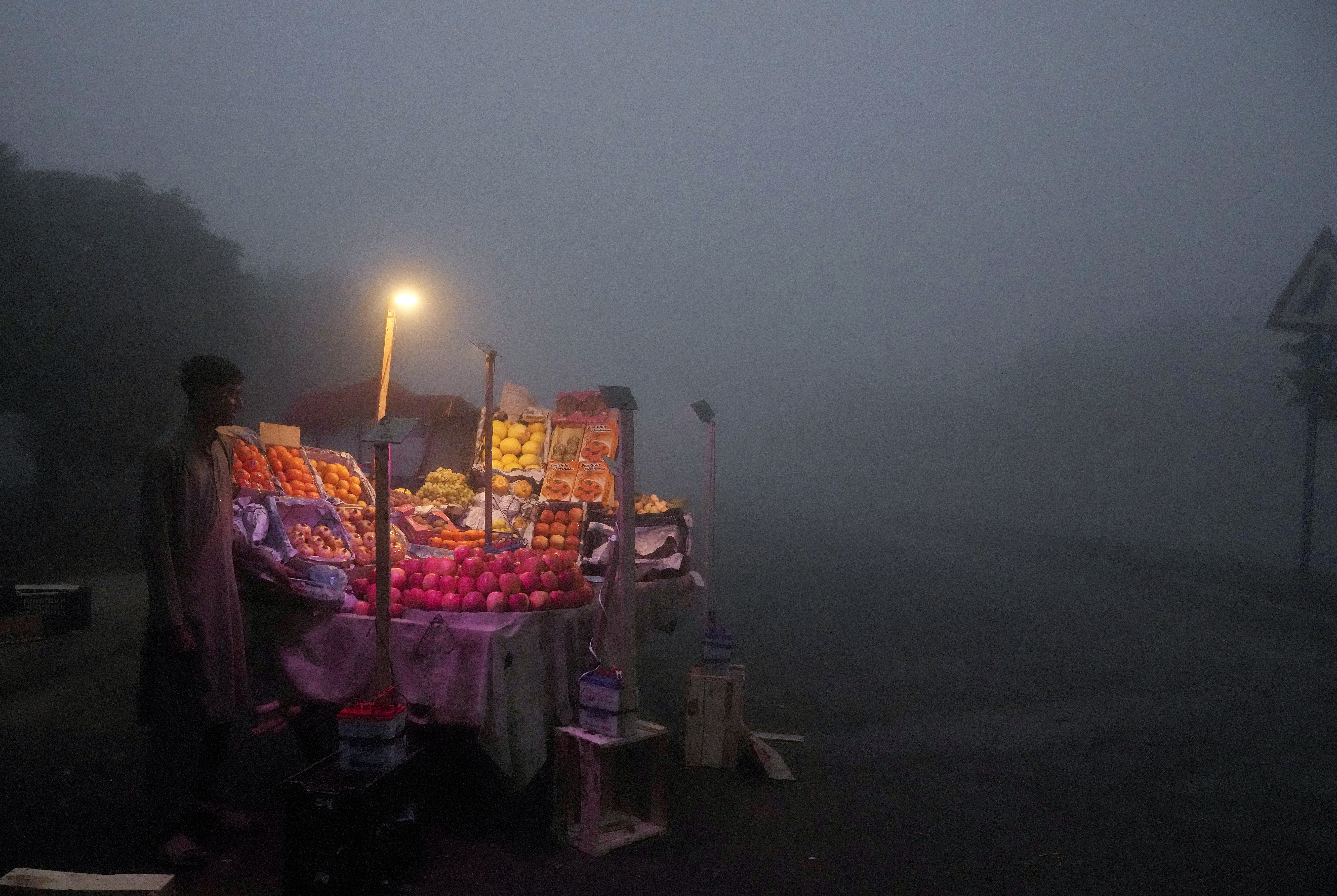 A fruit seller arranges his stall in the early morning as smog envelopes the area of Lahore, Pakistan, on Thursday, November 14, 2024 [KM Chaudary/AP]