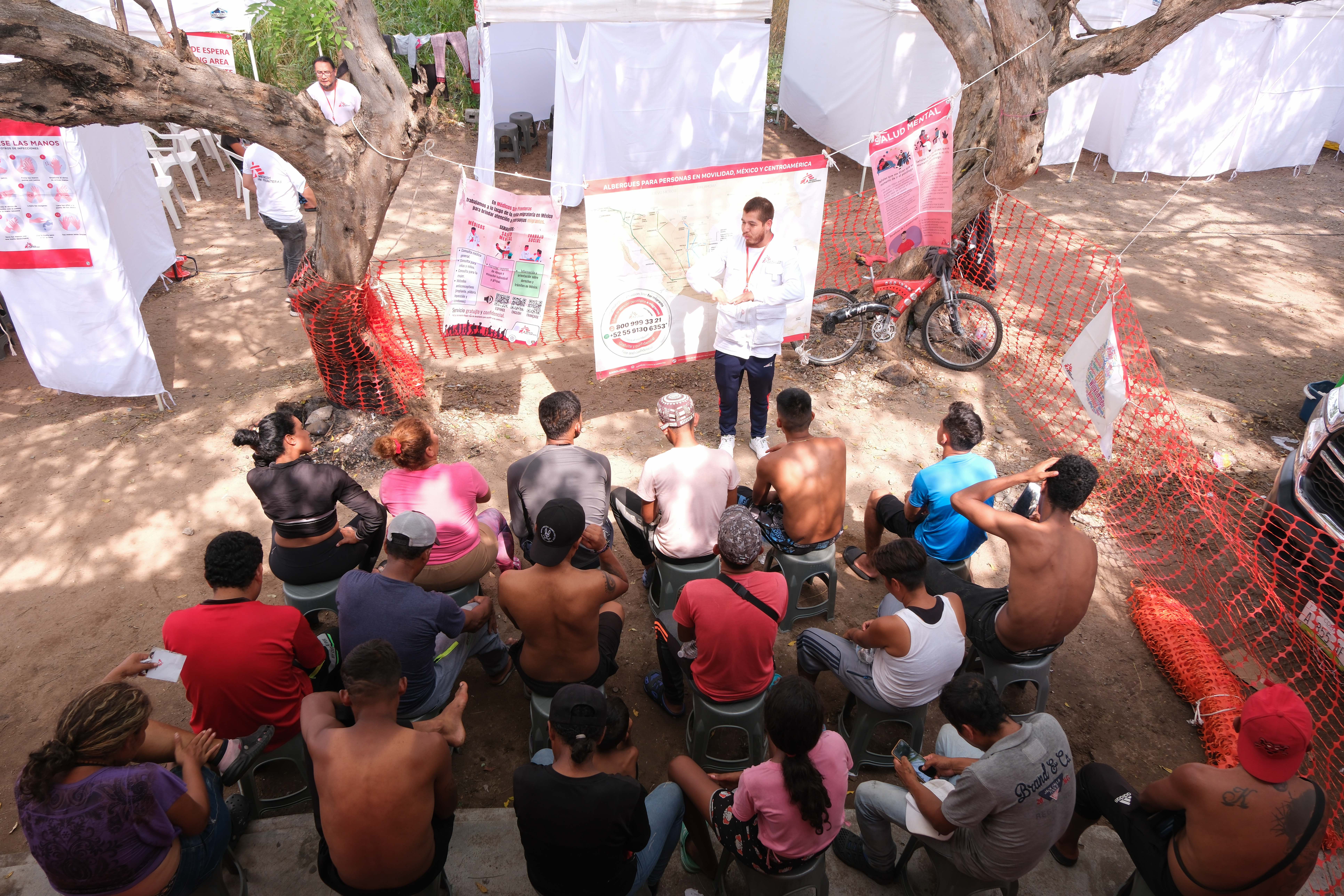 Migrants and asylum seekers sit around a Doctors Without Borders representative giving a presentation.