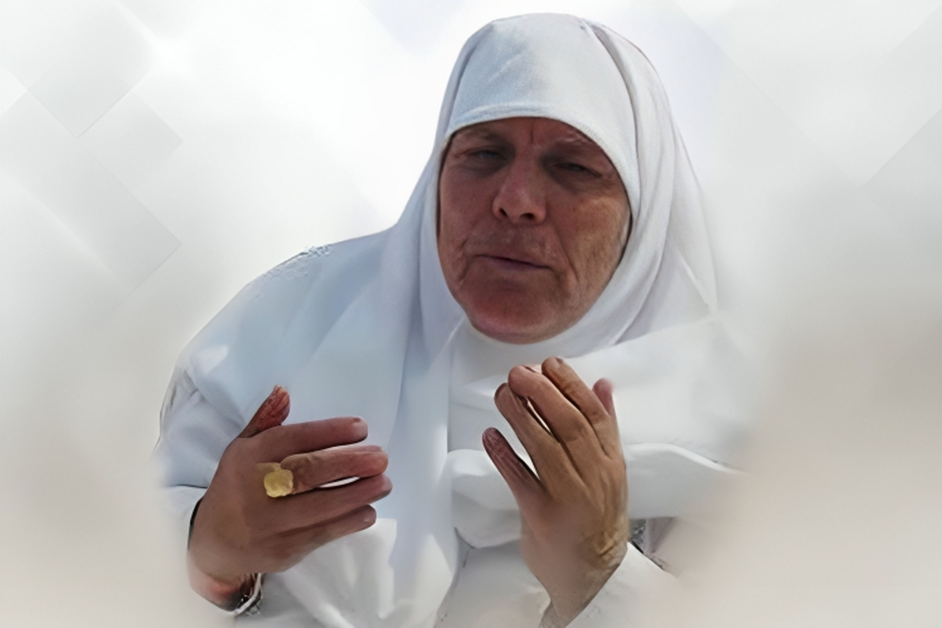 A photo of an elderly woman dressed in white hijab and gown