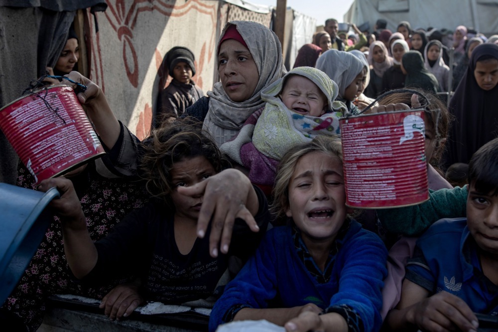 Palestinians, including children, hold metal pots and pans as they gather to receive food cooked by a charity kitchen.