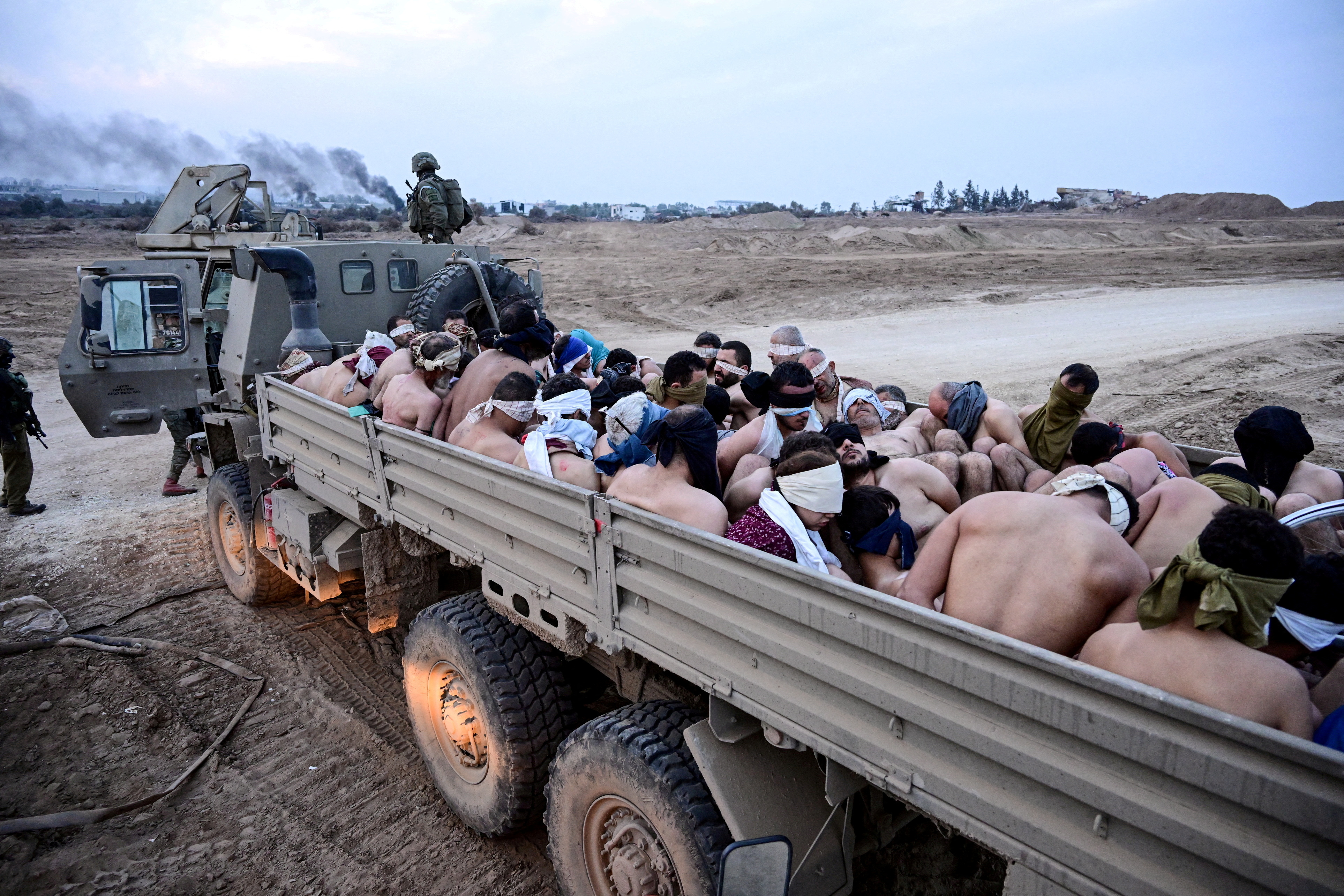 Israeli soldiers stand by a truck packed with shirtless Palestinian detainees.