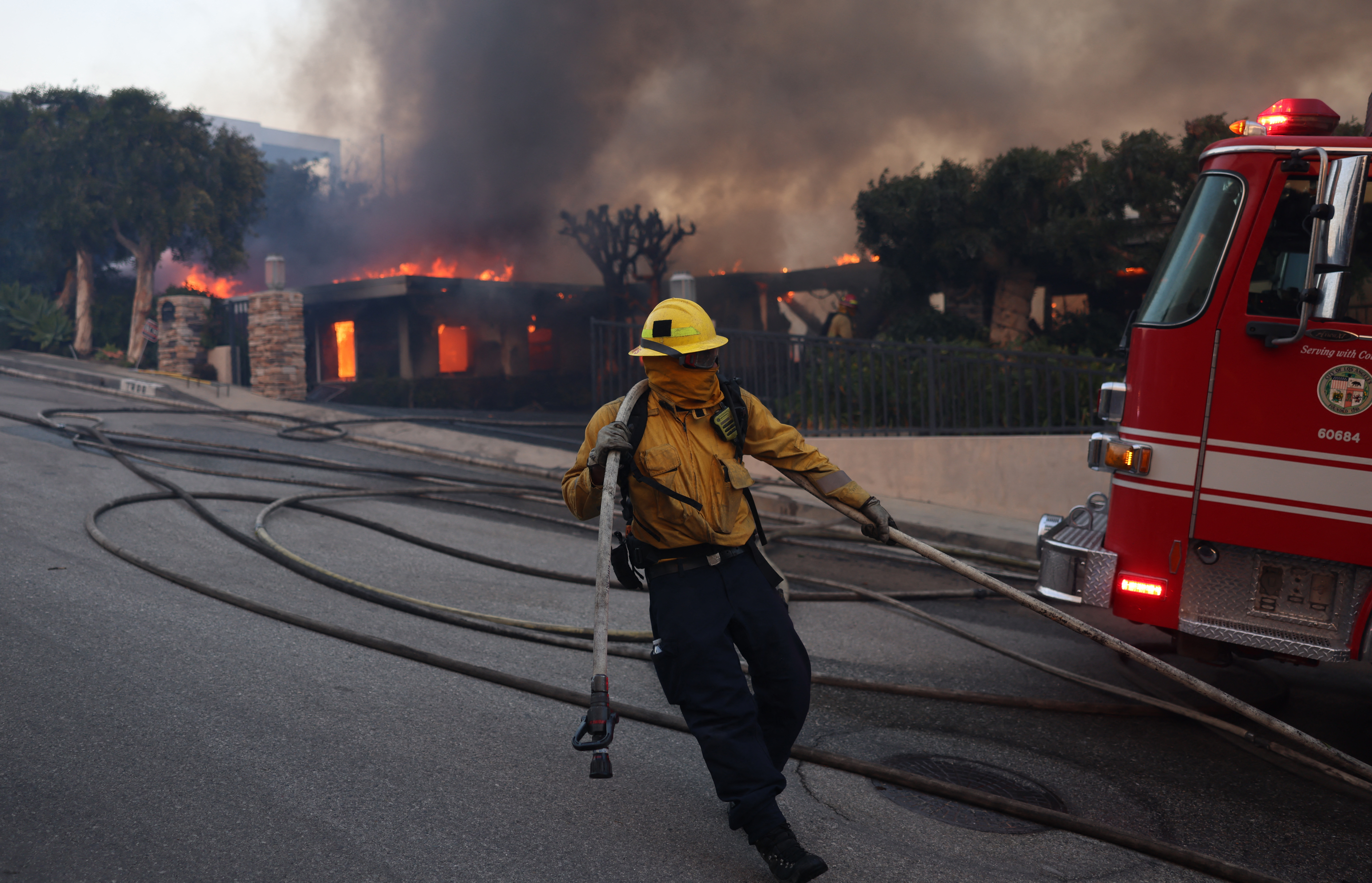 A firefighter drags a hose as a home is lost to the flames of the wind-driven Palisades Fire in Pacific Palisades, California, January 7