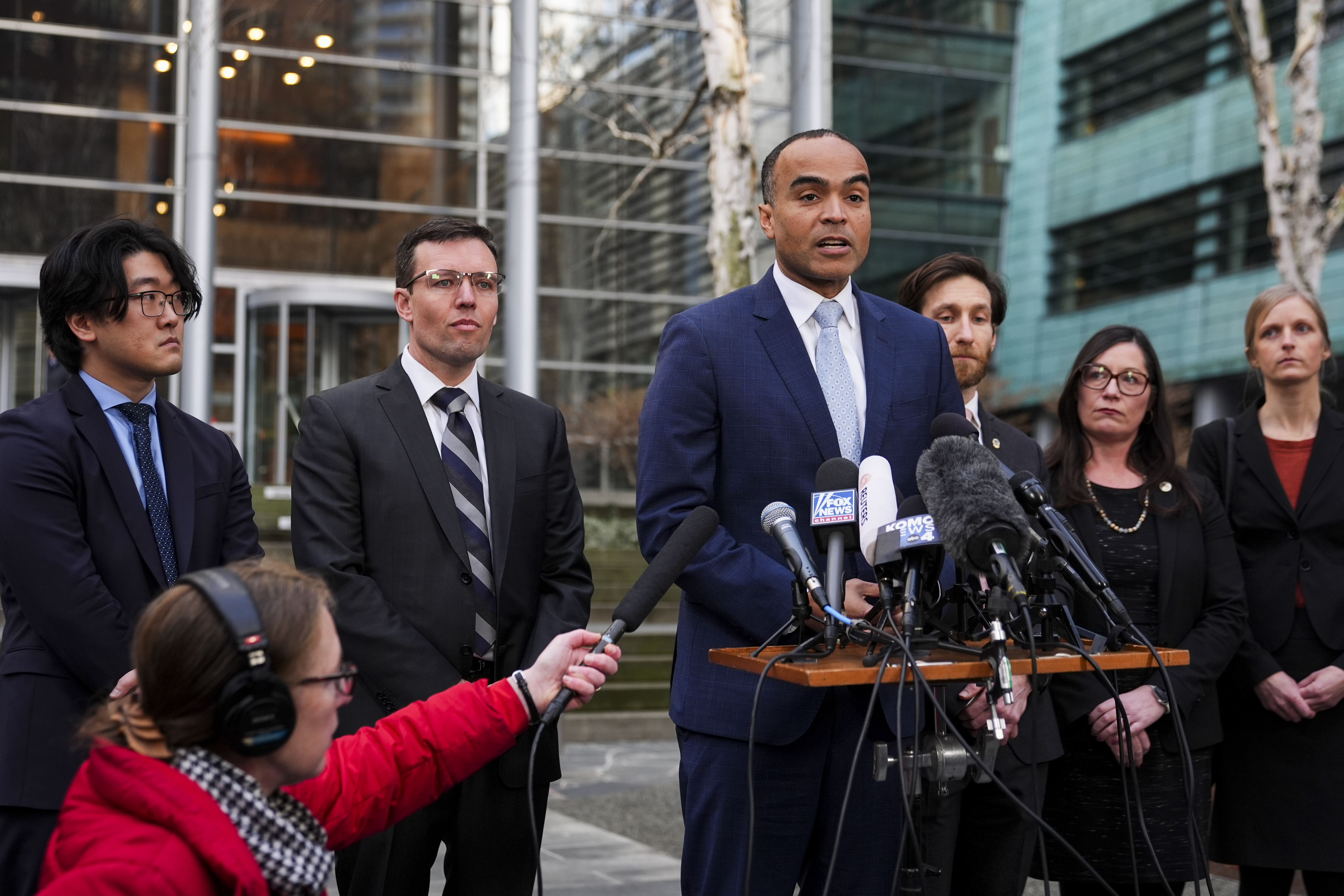 Washington Attorney General Nick Brown speaks at an outdoor podium, surrounded by reporters.