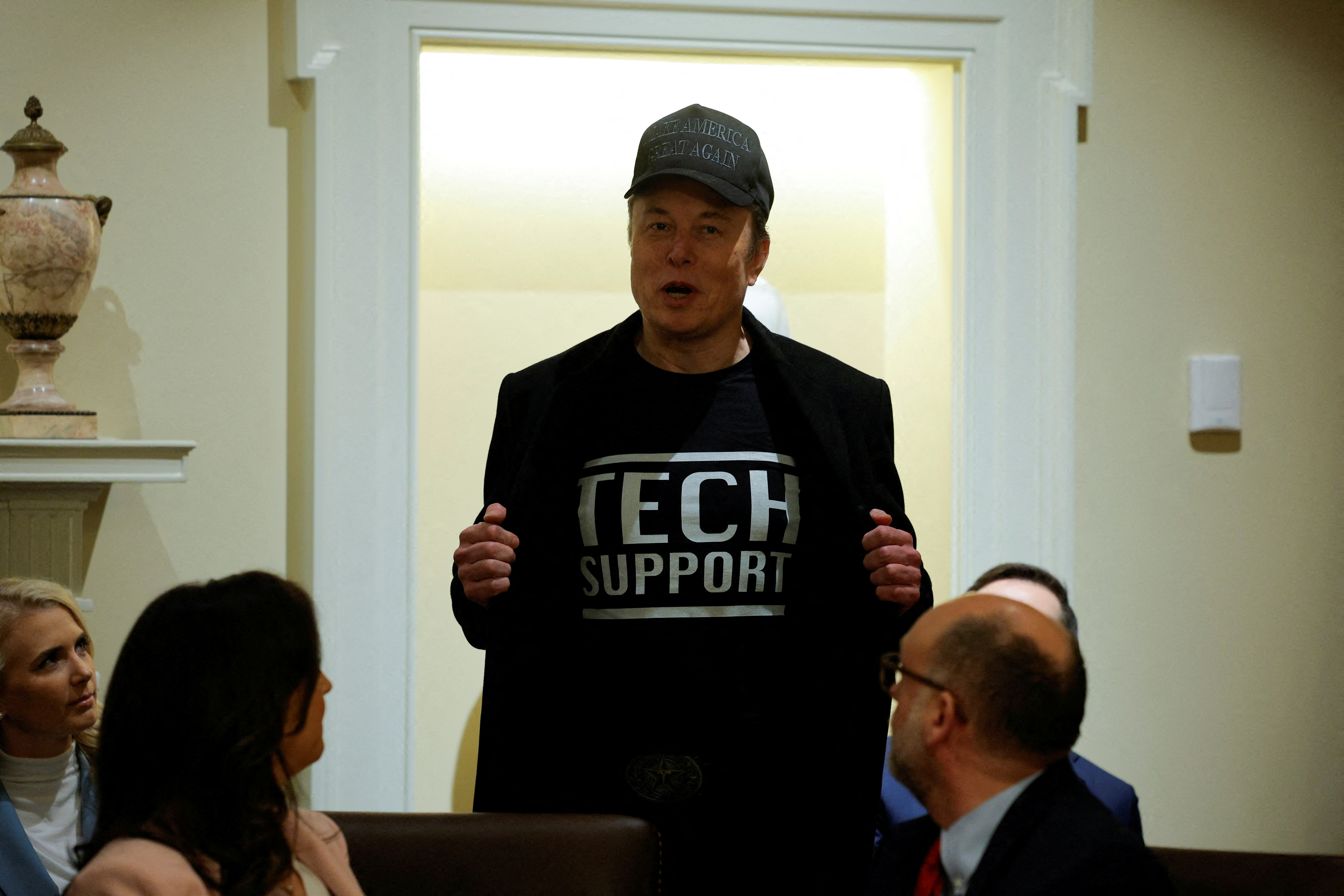 Elon Musk opens his blazer to reveal a shirt that reads "Tech support"