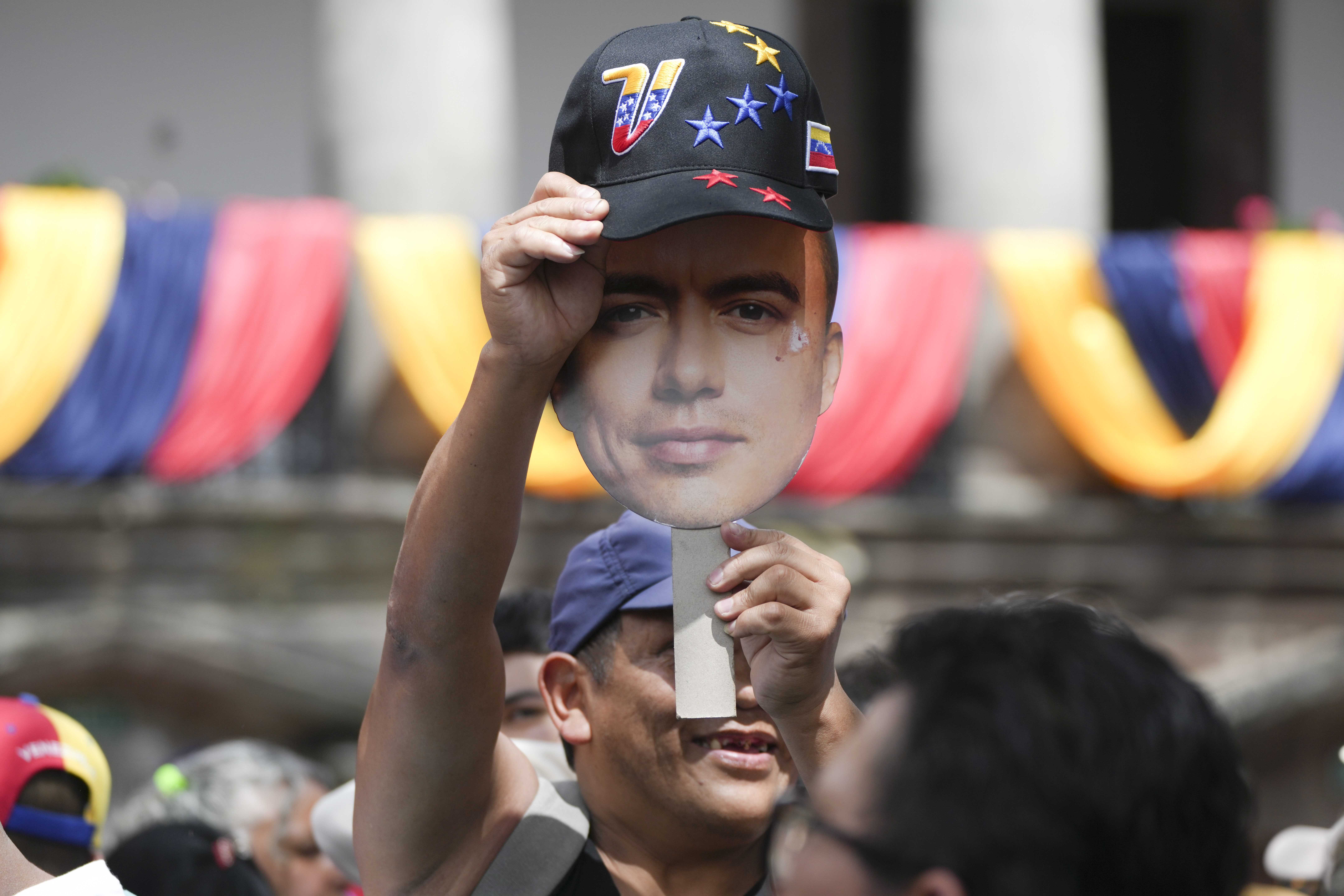 A supporter holds up a cut-out of Daniel Noboa's head and holds a baseball cap over it.