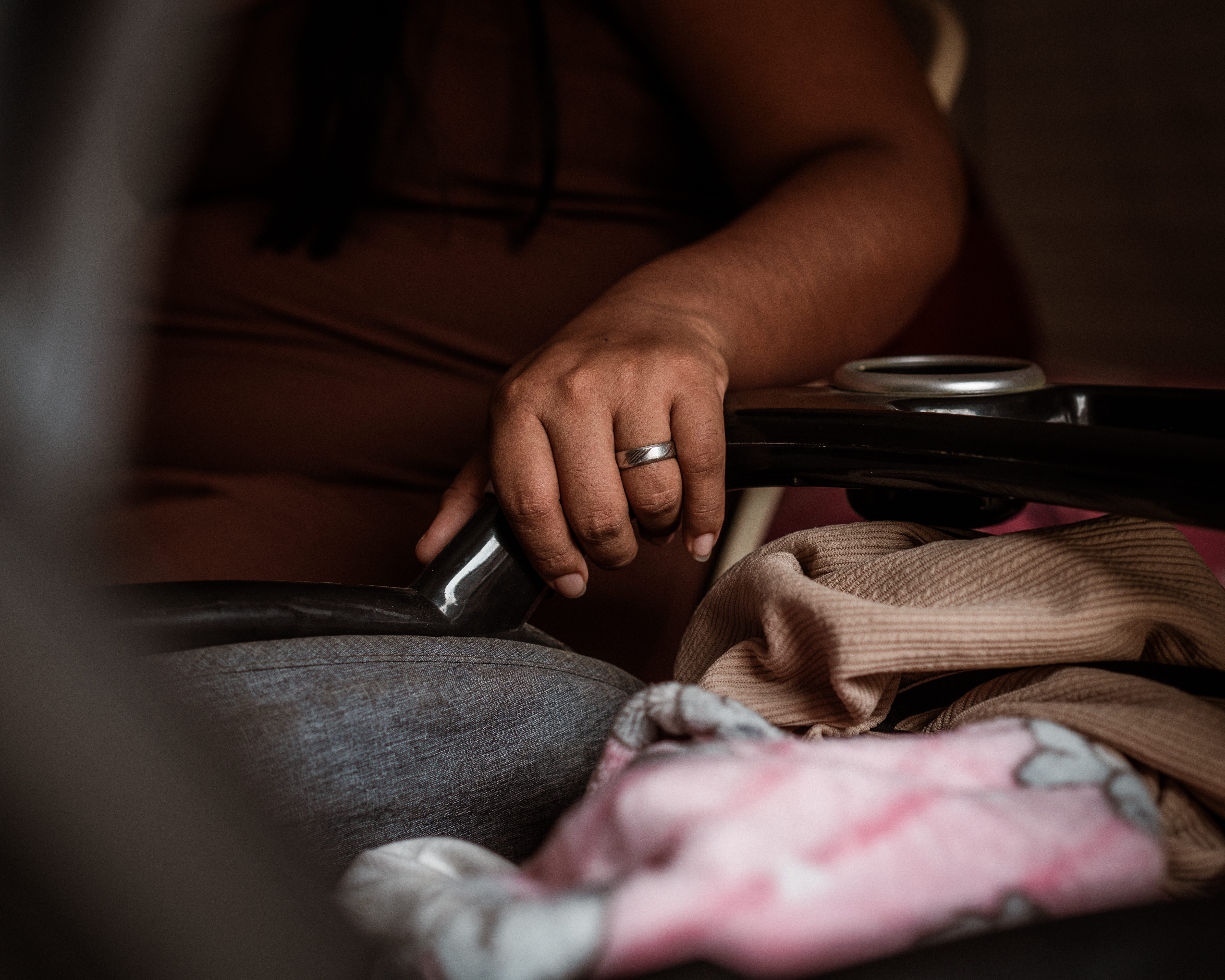 A 26-year-old mother rocks her newborn child in a stroller, a silver wedding band visible on her finger.