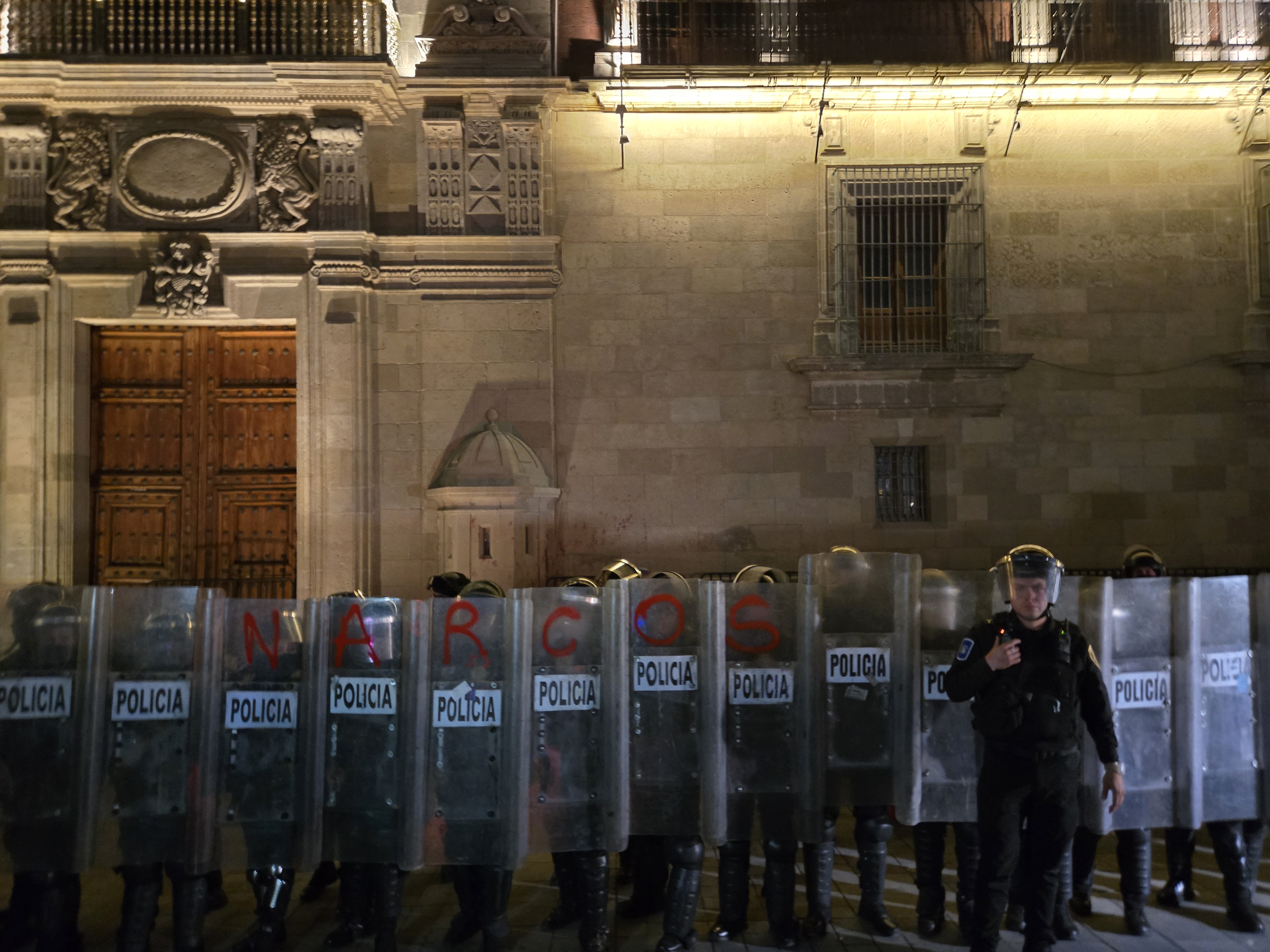 Police stand guard outside the National Palace in Mexico City, their riot shields spray-painted with the word