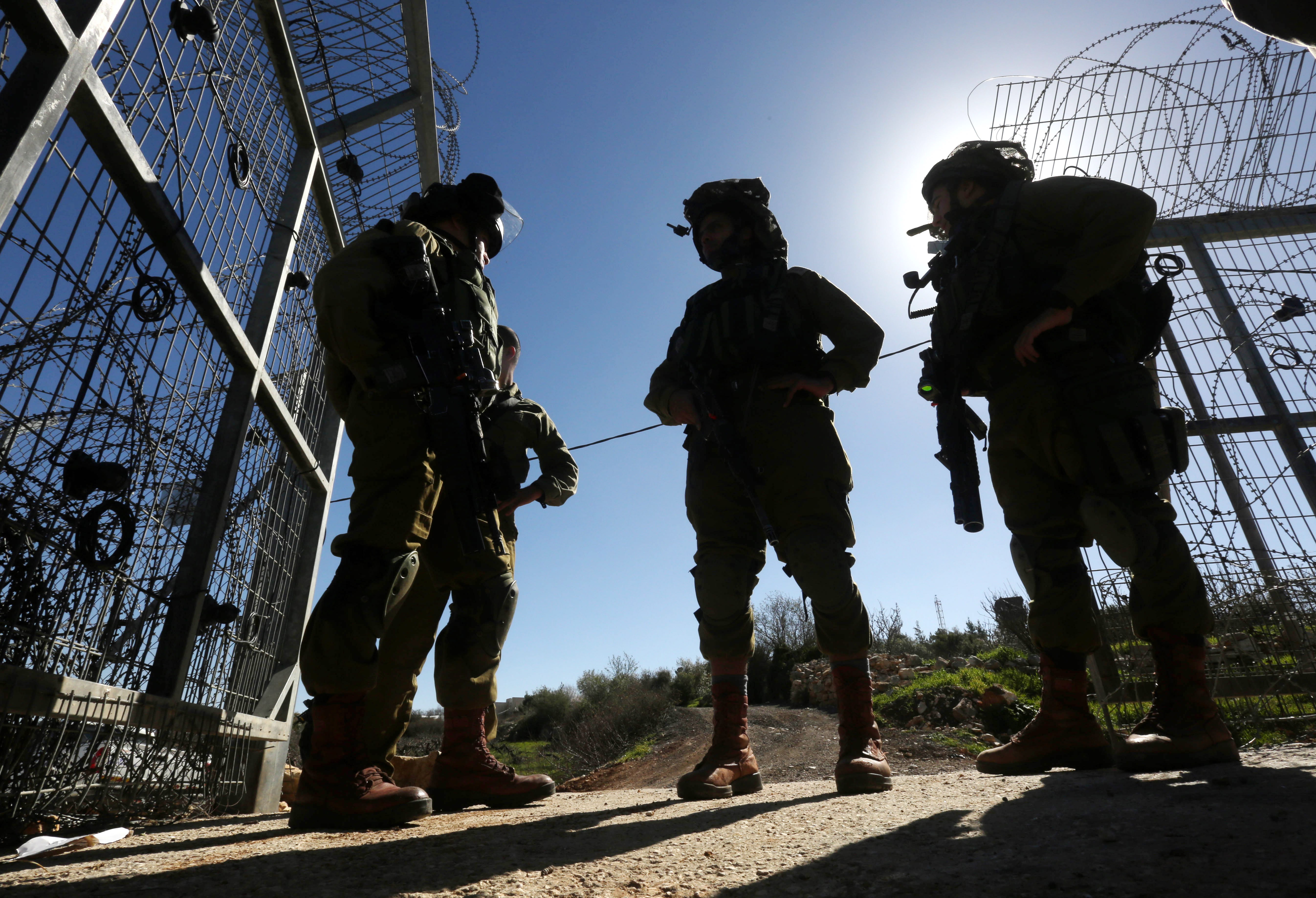 Heavily armed Israeli soldiers at a barbed-wire barrier.