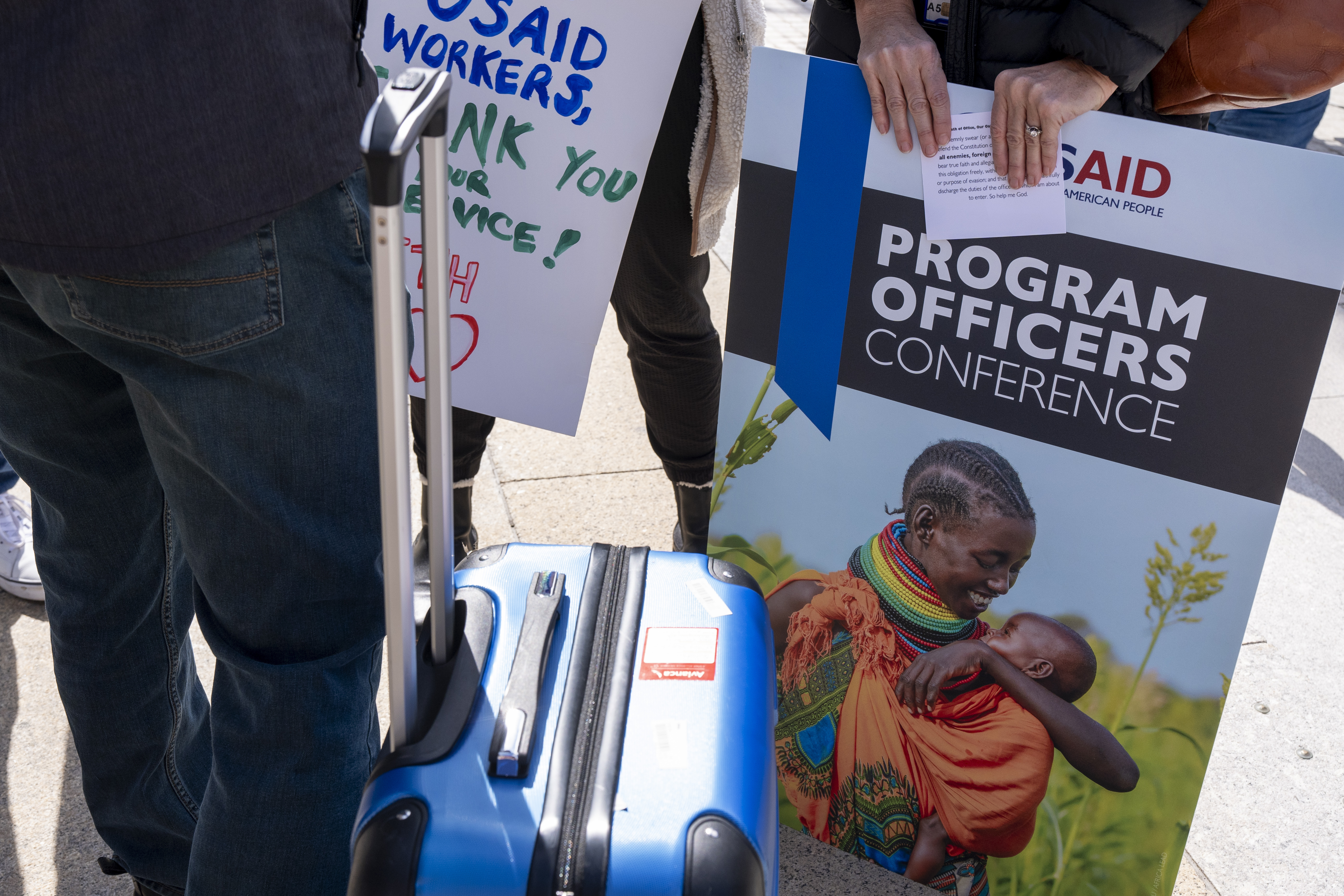 A laid off USAID employee holds a poster of her work, her oath of office, and a suitcase full of personal items, Friday, Feb. 28, 2025, after being given 15 minutes to clear out their items from USAID Headquarters in Washington. (AP Photo/Jacquelyn Martin)
