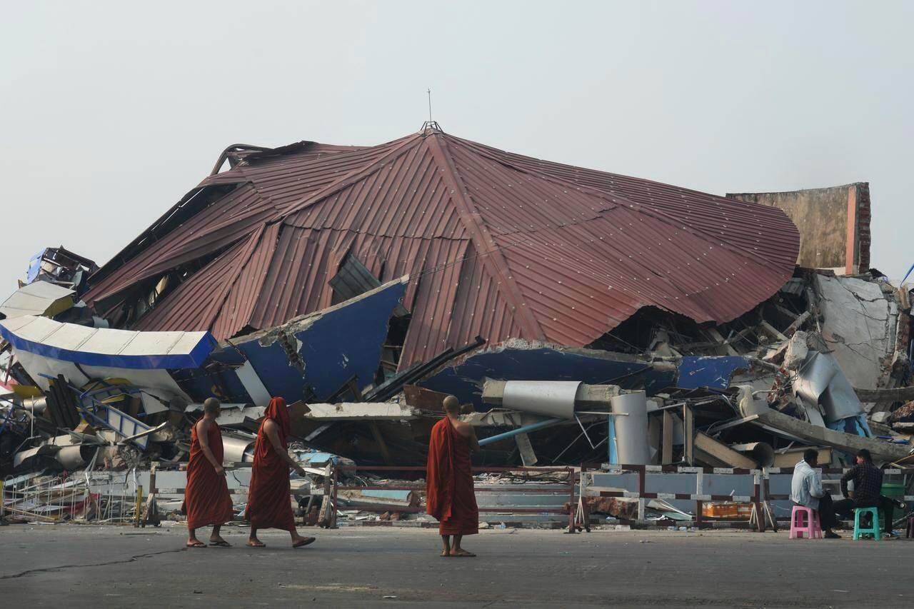 Buddhist monks walk past a collapsed building after a powerful earthquake.