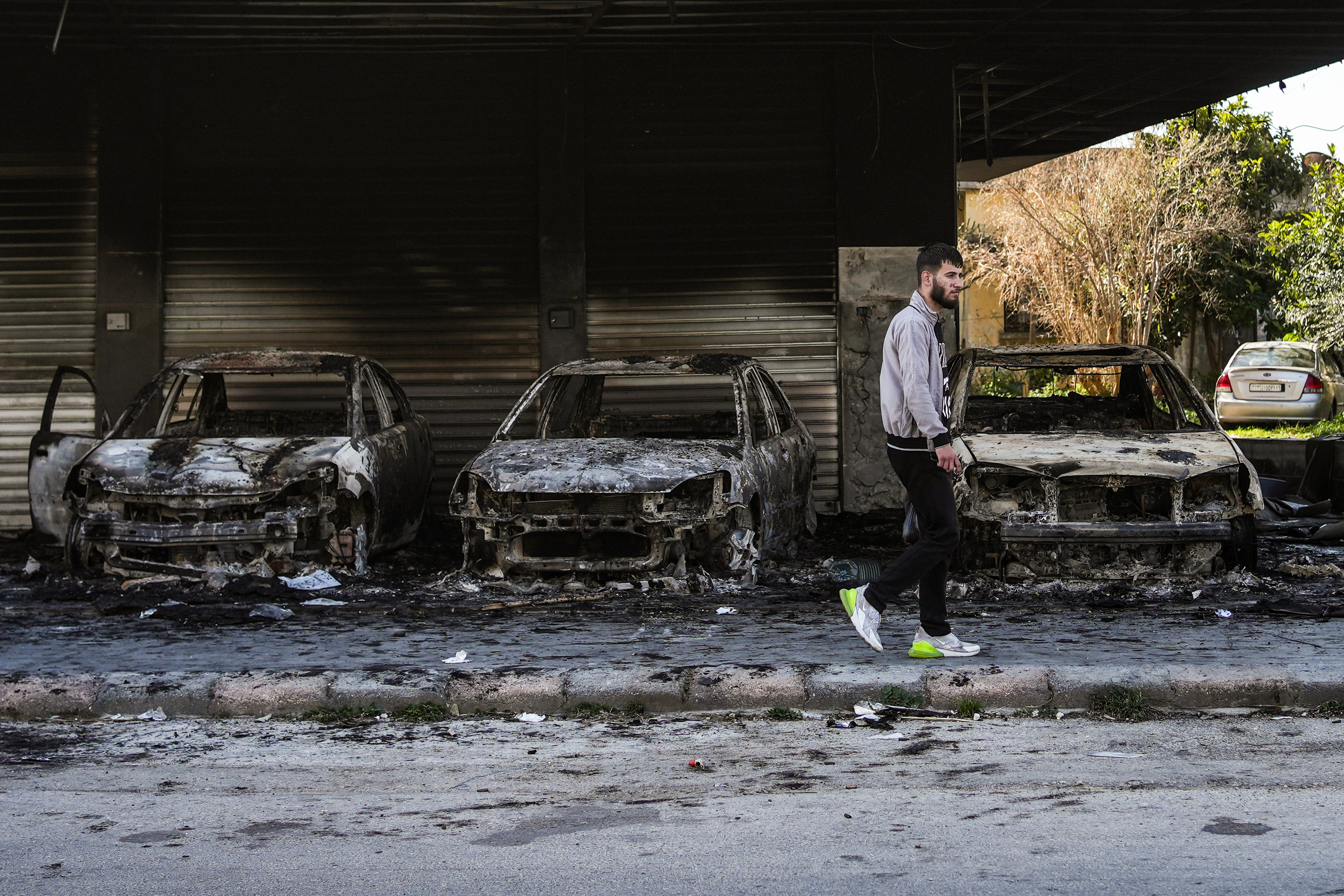 A Syrian man walks past burnt out cars on a street in Jableh town