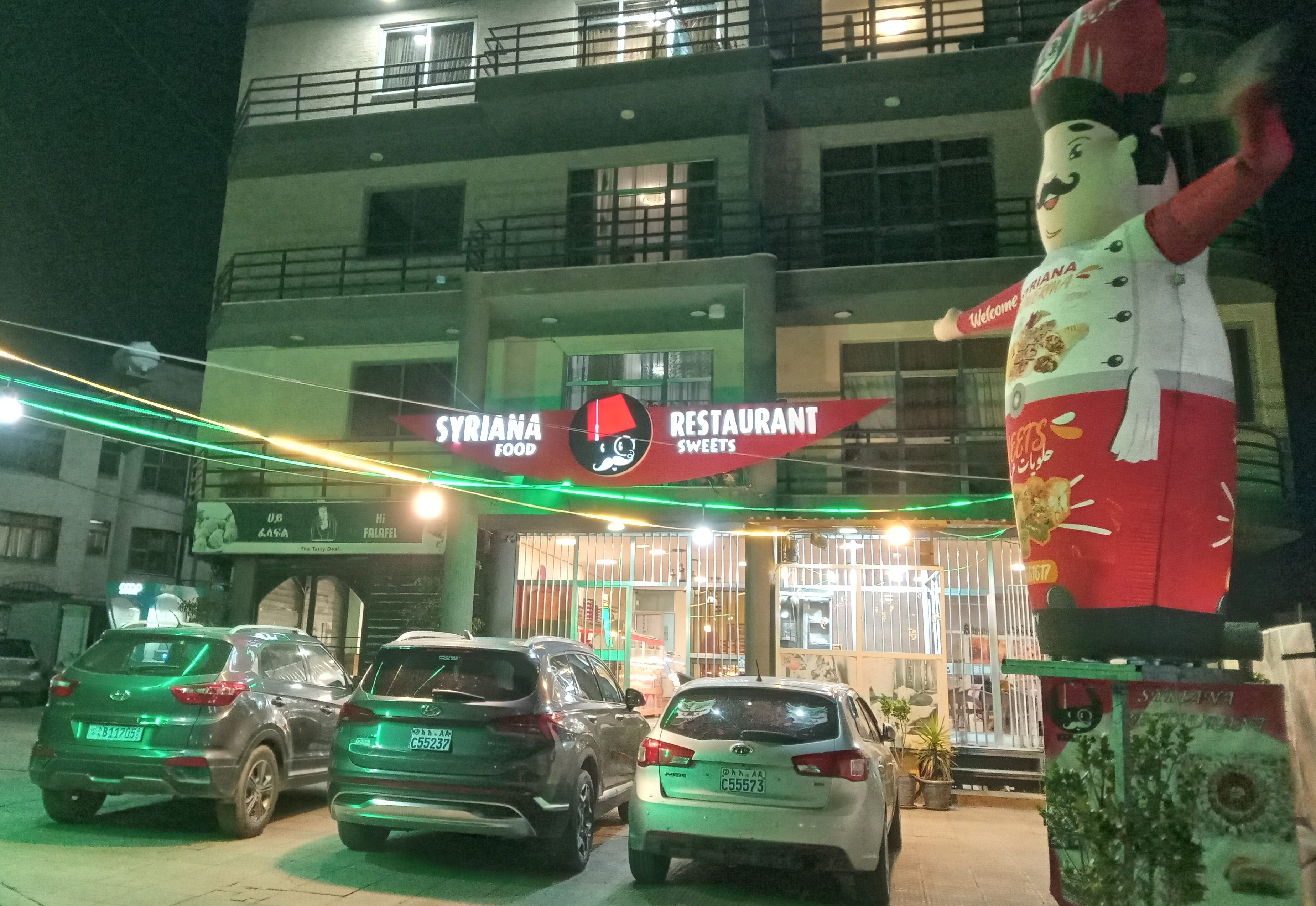 residential building with a restaurant on the ground floor, with cars parked in front and an inflatable dancer streetside