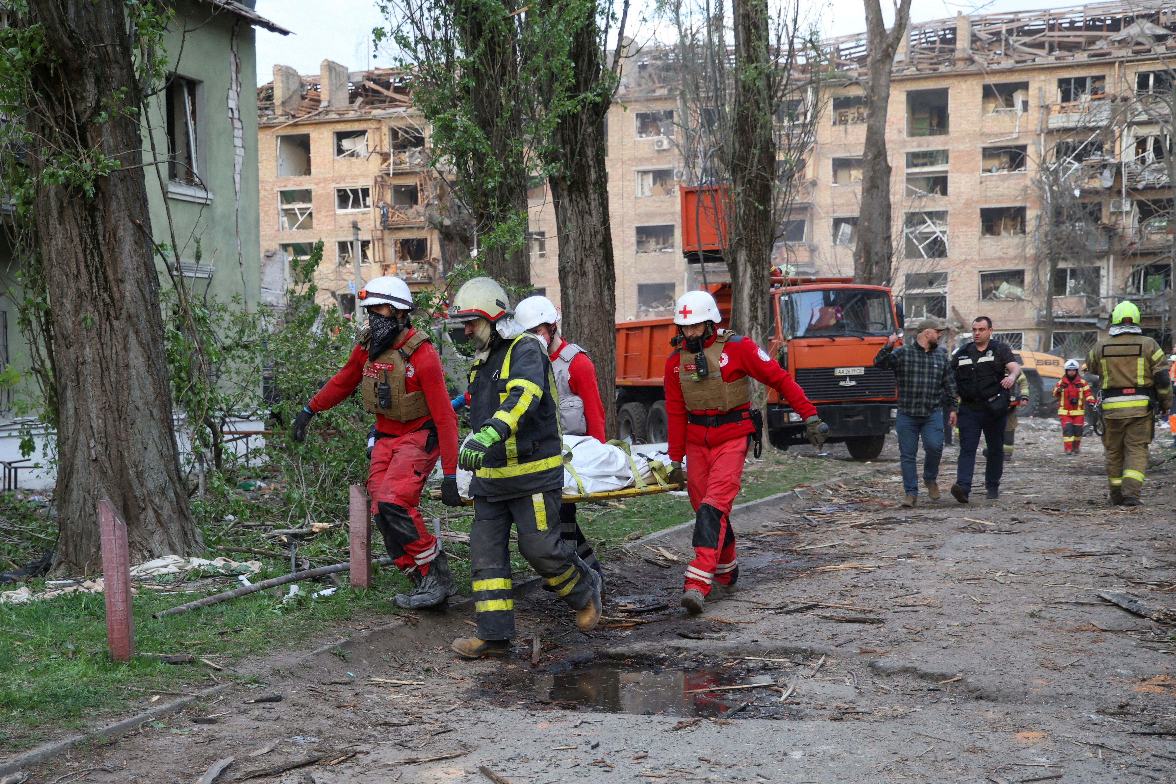 Paramedics and a rescuer carry the body of a person found under debris of an apartment building.