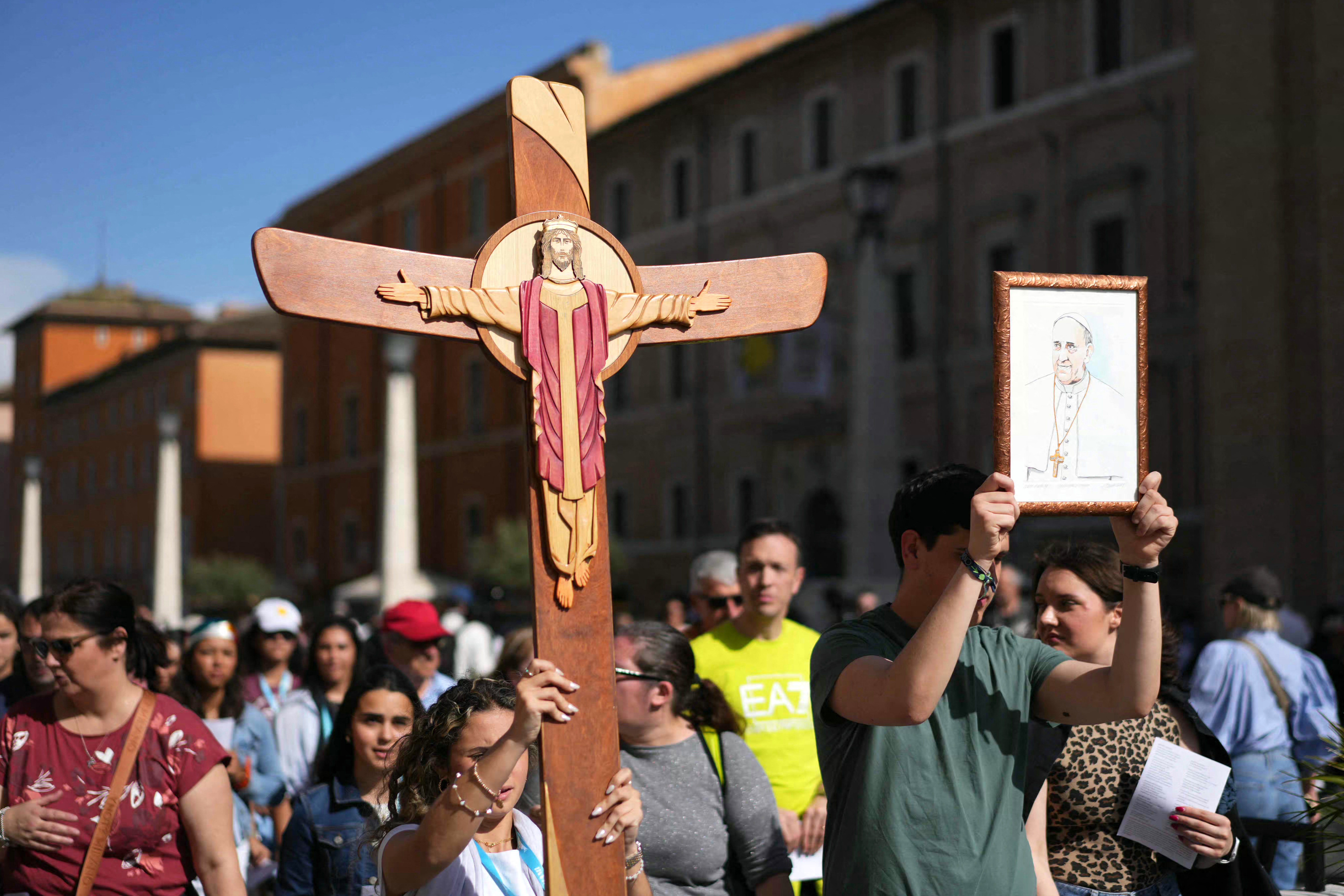 Pilgrims walk behind others holding a cross and portrait of the late Pope Francis