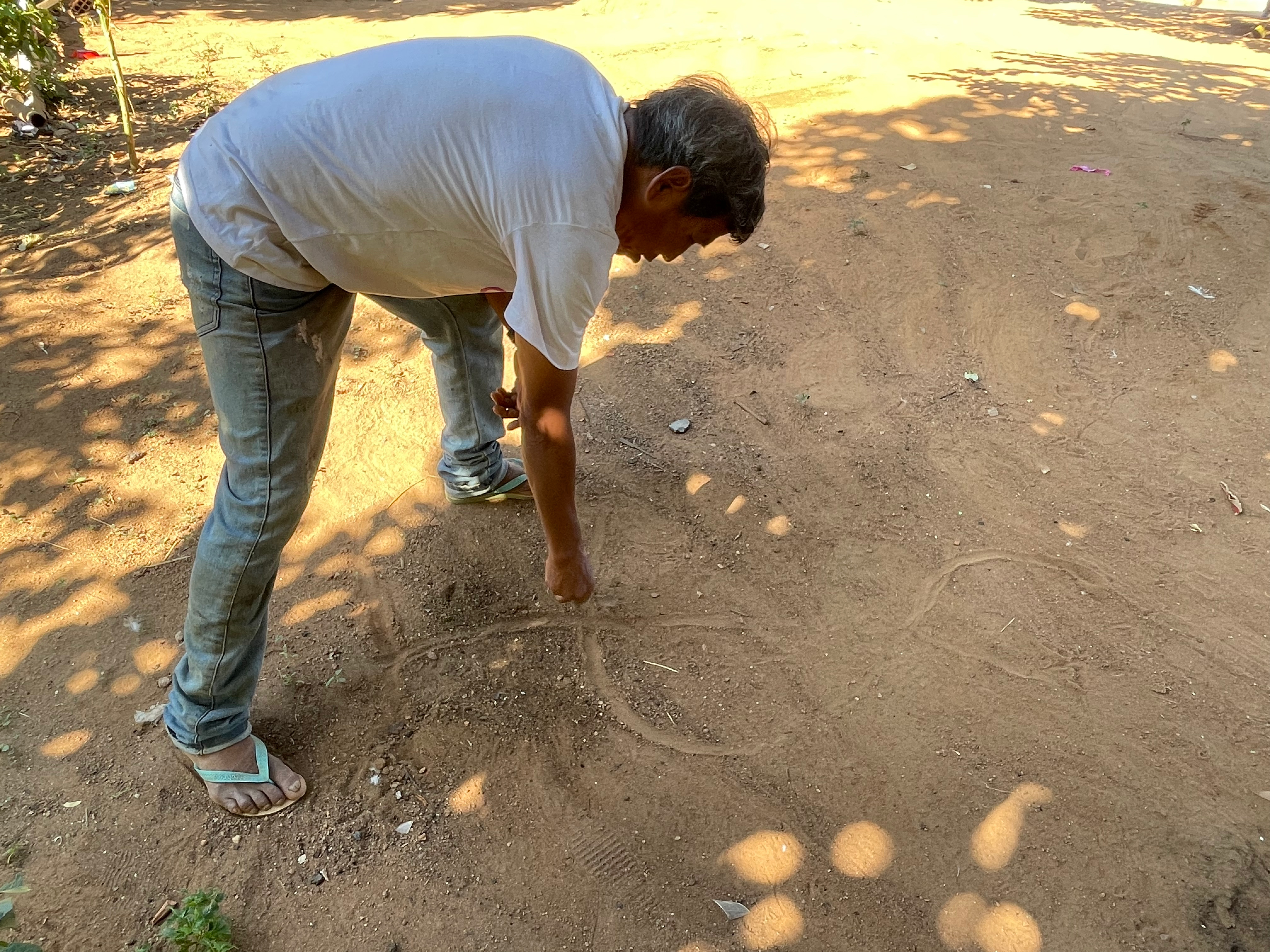Damasio Maxakali leans over and draws in the dirt to show how the environment has changed.