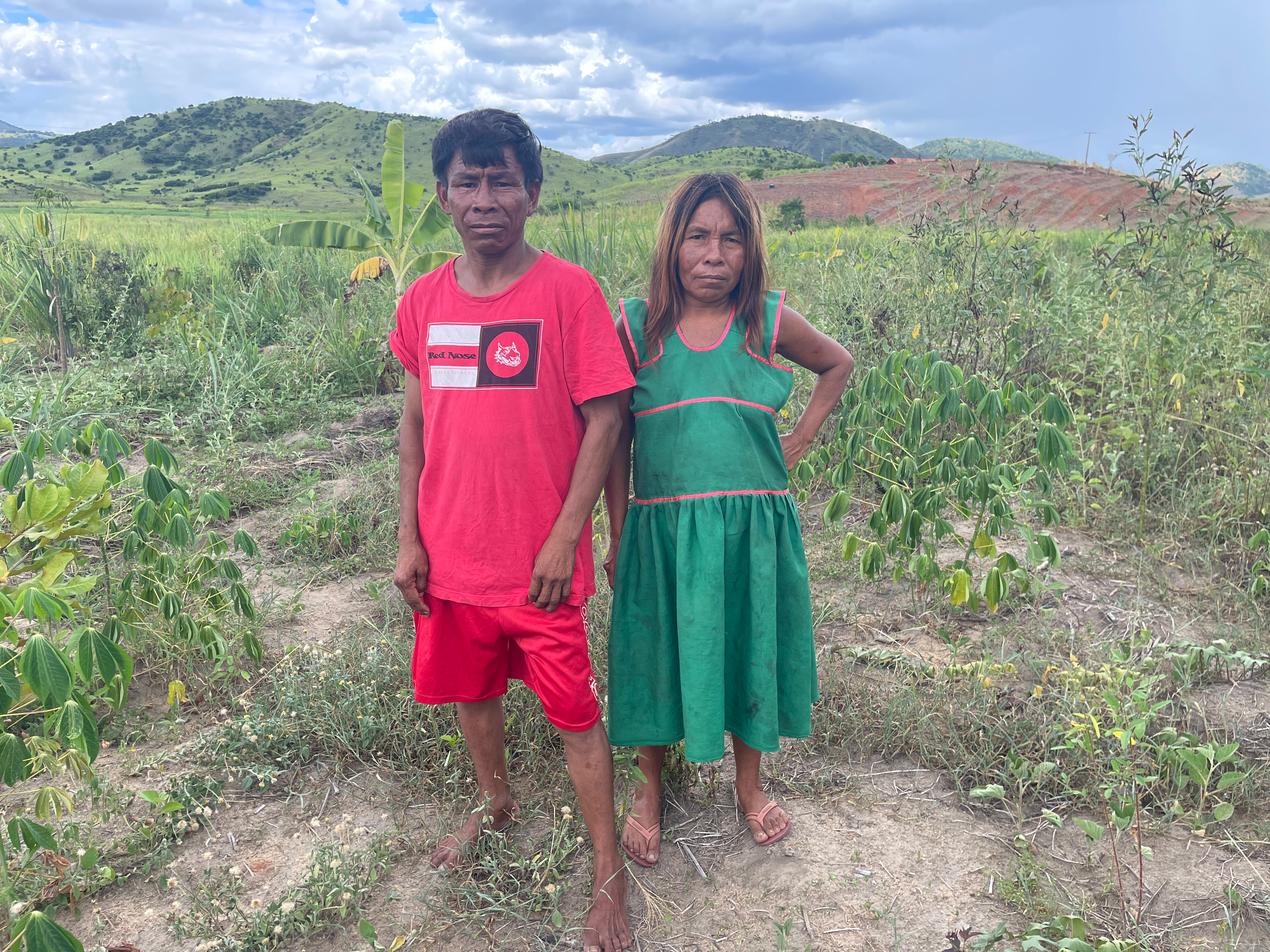 Two Maxakali Indigenous people — a man and a woman — stand in front of a verdant landscape
