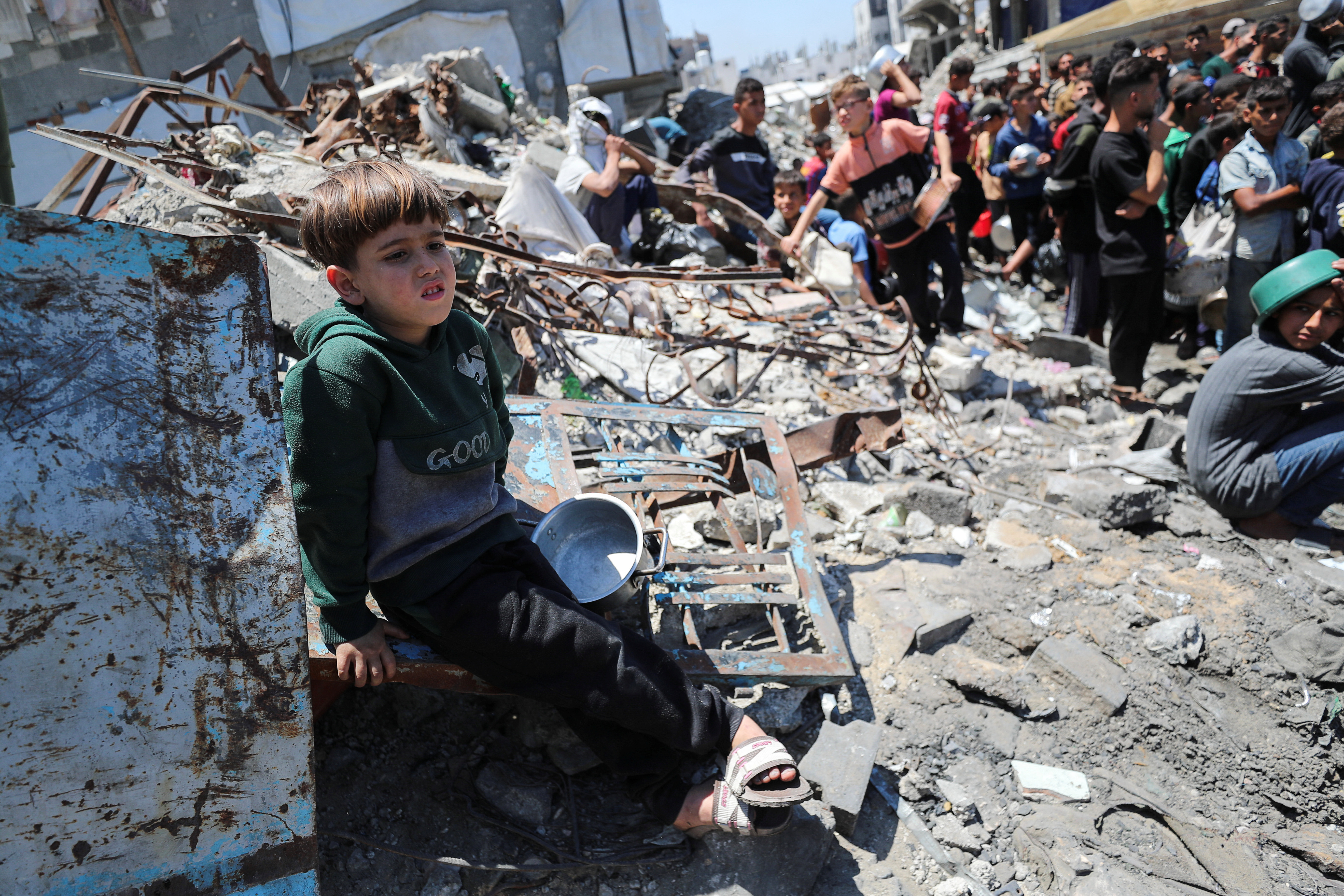 A child sits, as Palestinians wait to receive food cooked by a charity kitchen, in Beit Lahia, northern Gaza Strip, May 8, 2025. REUTERS/Mahmoud Issa
