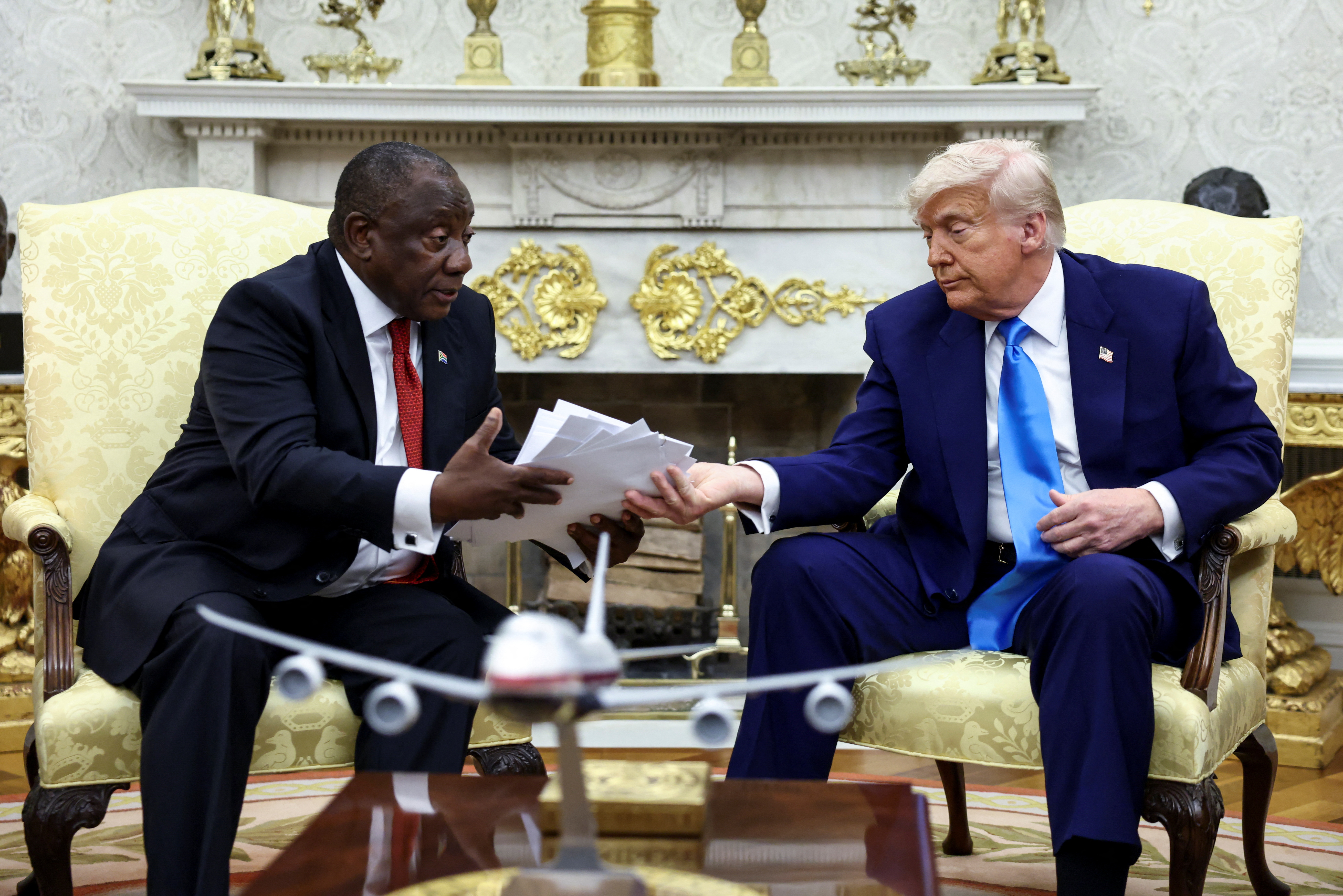 U.S. President Donald Trump hands over to South African President Cyril Ramaphosa copies of articles that he said showed white South Africans who had been killed, in the Oval Office of the White House in Washington, D.C., U.S., May 21, 2025