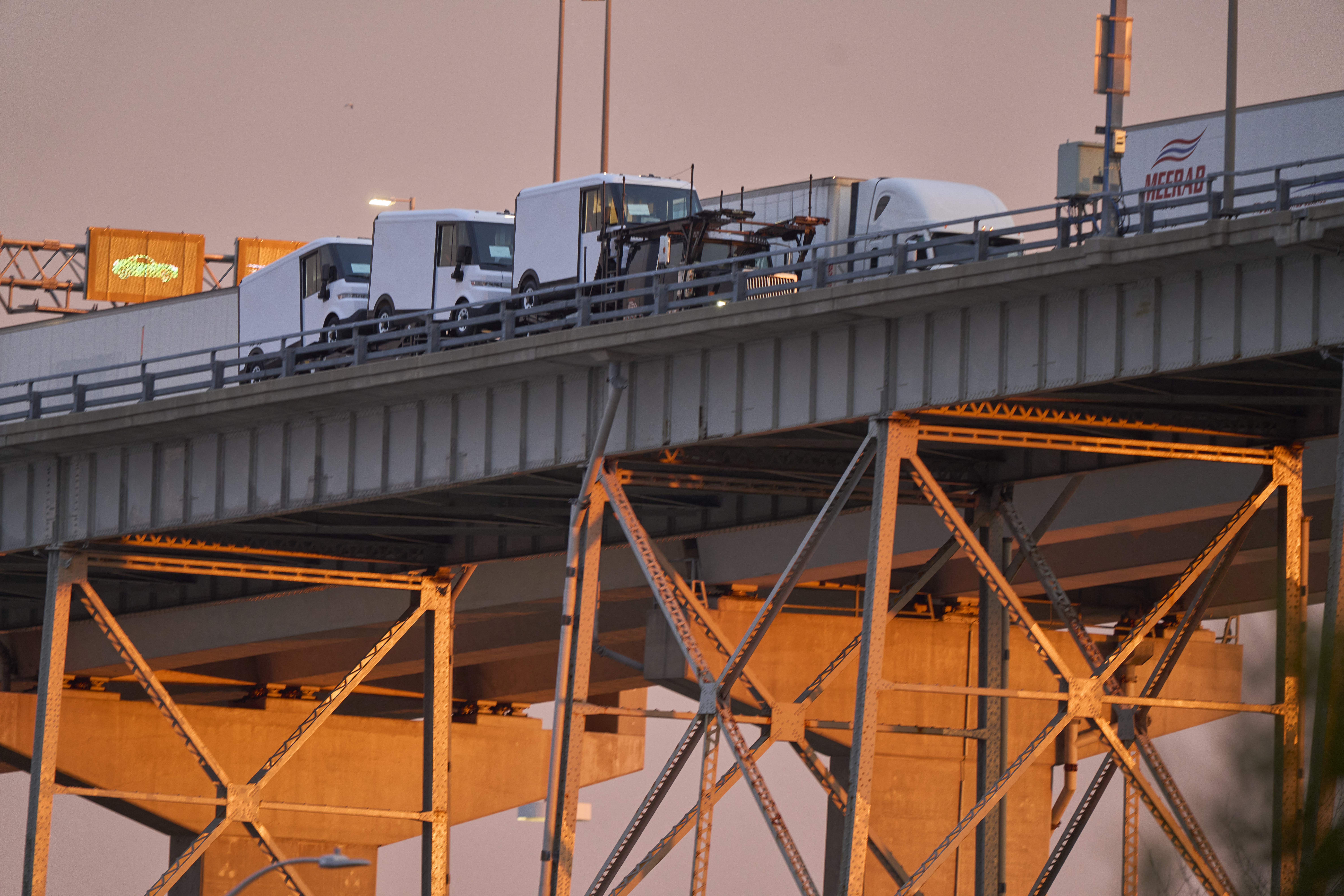 A transport truck carrying electric delivery vans crosses a bridge.