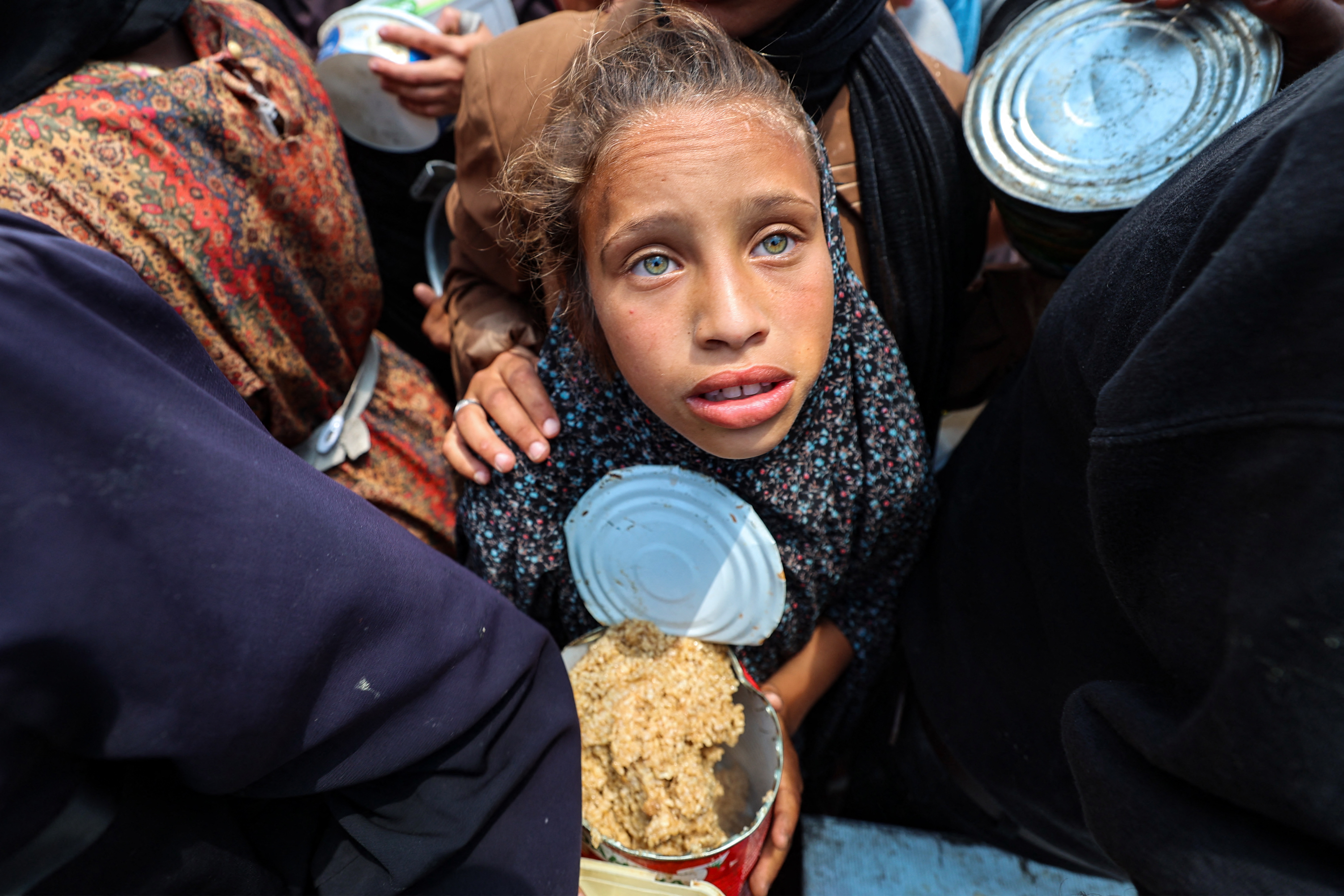 A Palestinian girl holds a container at a food distribution point in the Nuseirat camp